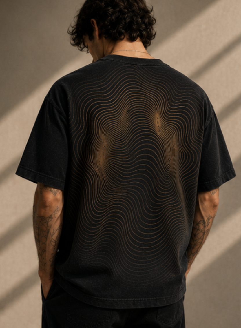 Back view of a man with curly hair wearing a black T-shirt with a gold geometric line pattern.