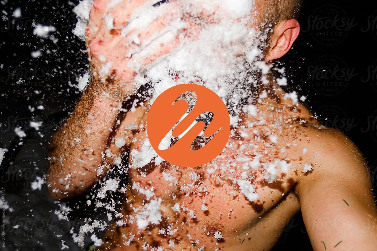 A person throwing white powder, possibly flour or powdered sugar, into the air with a black background.