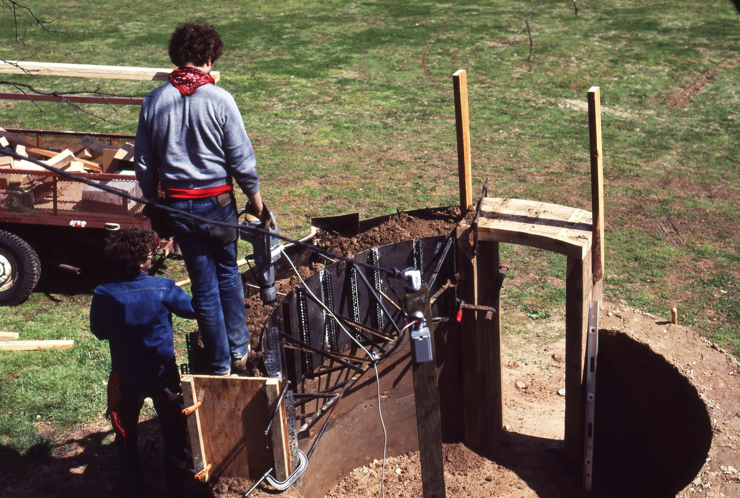 Two people working together on a construction project outdoors, assembling a concrete wall or foundation with wooden and metal supports.