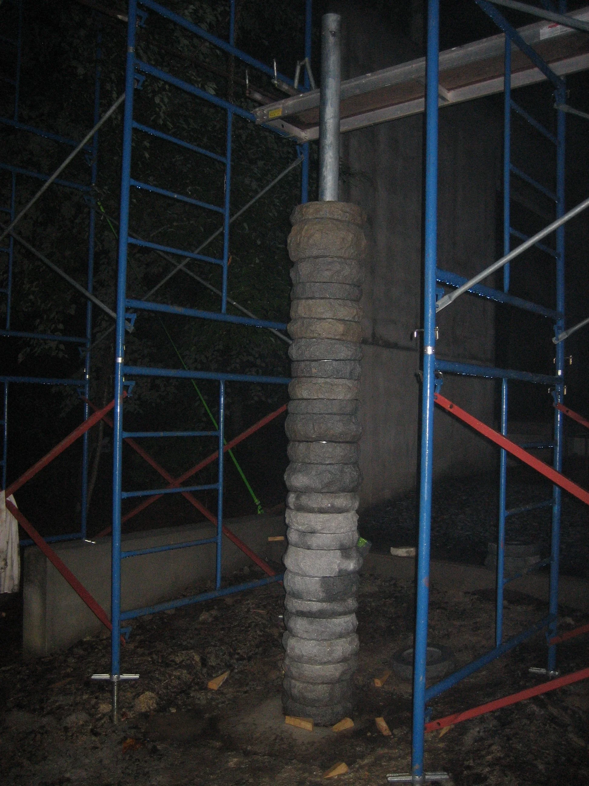 Construction site with metal scaffolding and a stack of grey bricks around a metal pole.