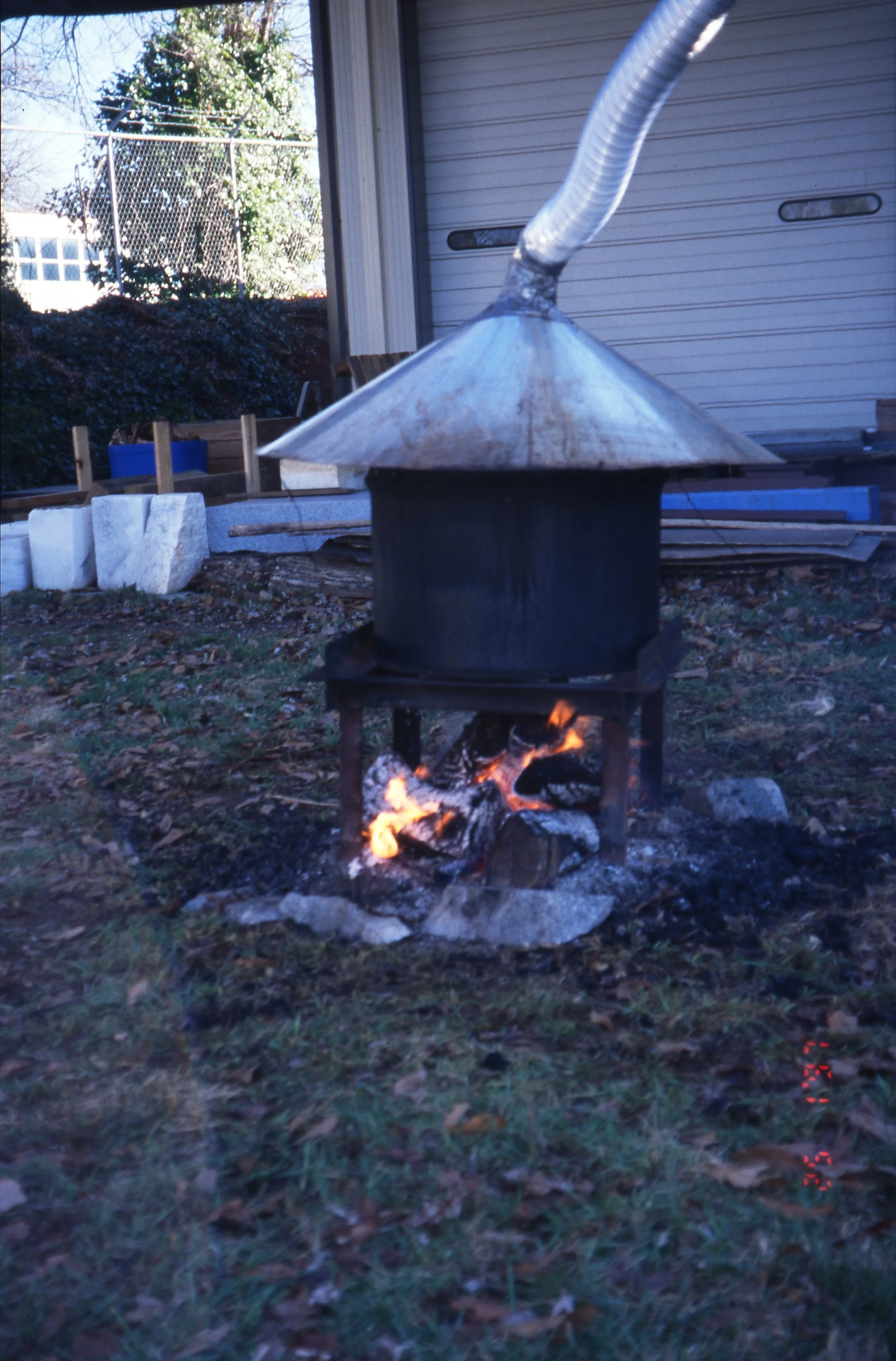 A small outdoor stove with a metal dome roof and a clear plastic pipe coming out, with wood burning underneath and small flames visible.