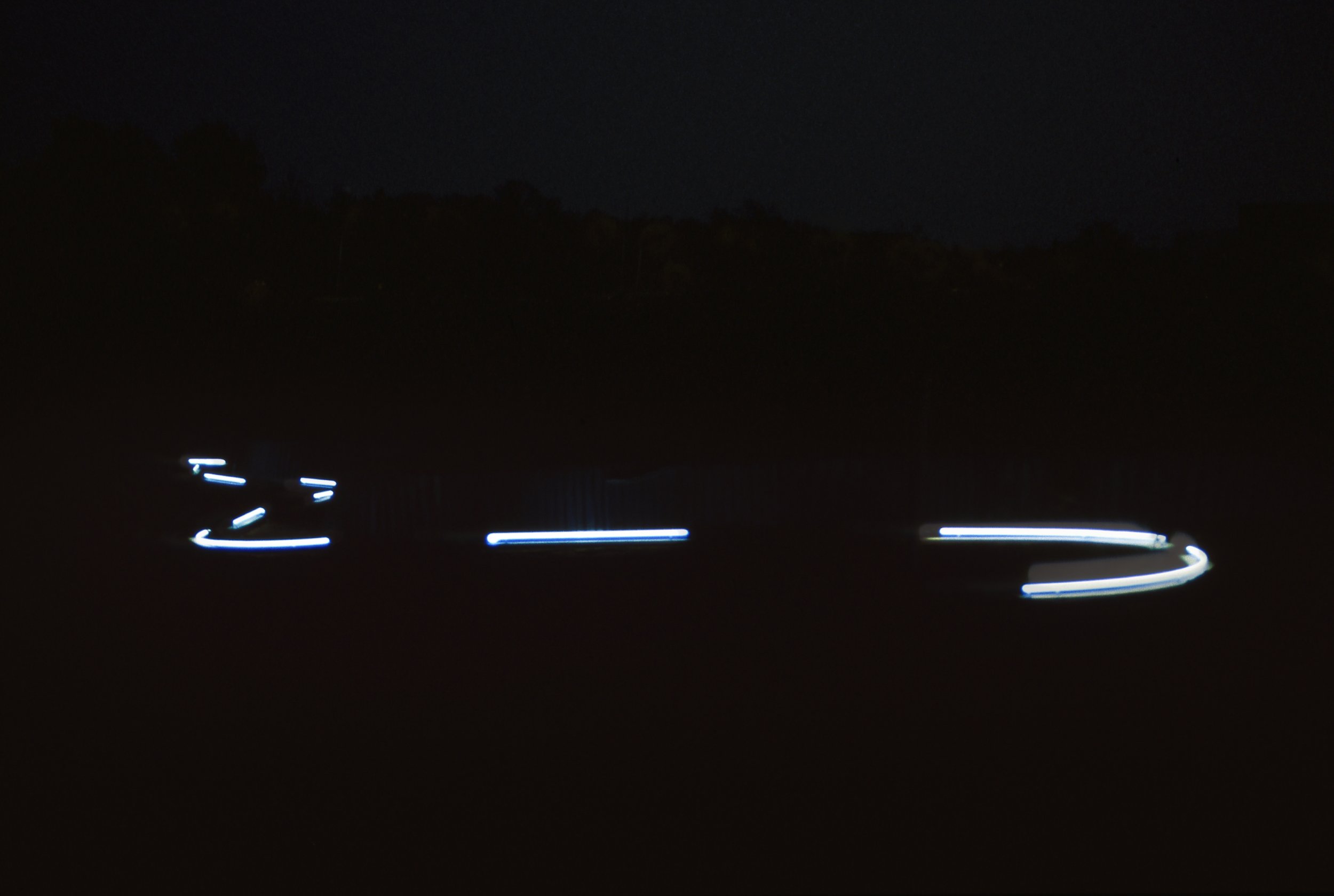 Light trails created by moving vehicle lights on a dark road at night, with a silhouette of a mountain range in the background.