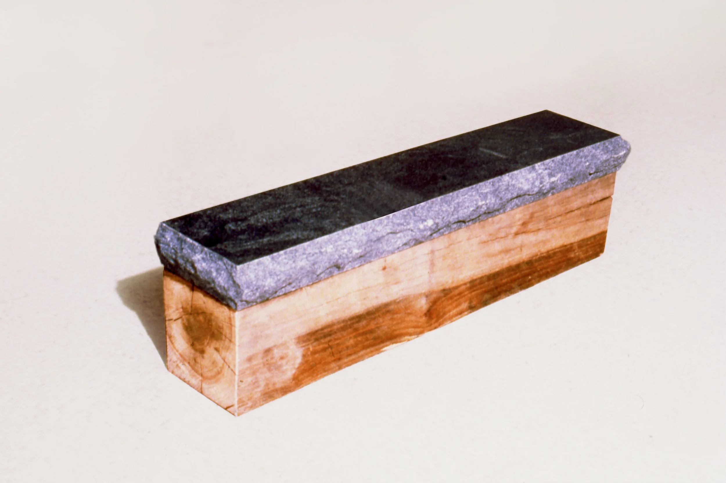 A small rectangular object with a wooden base and a dark stone top.