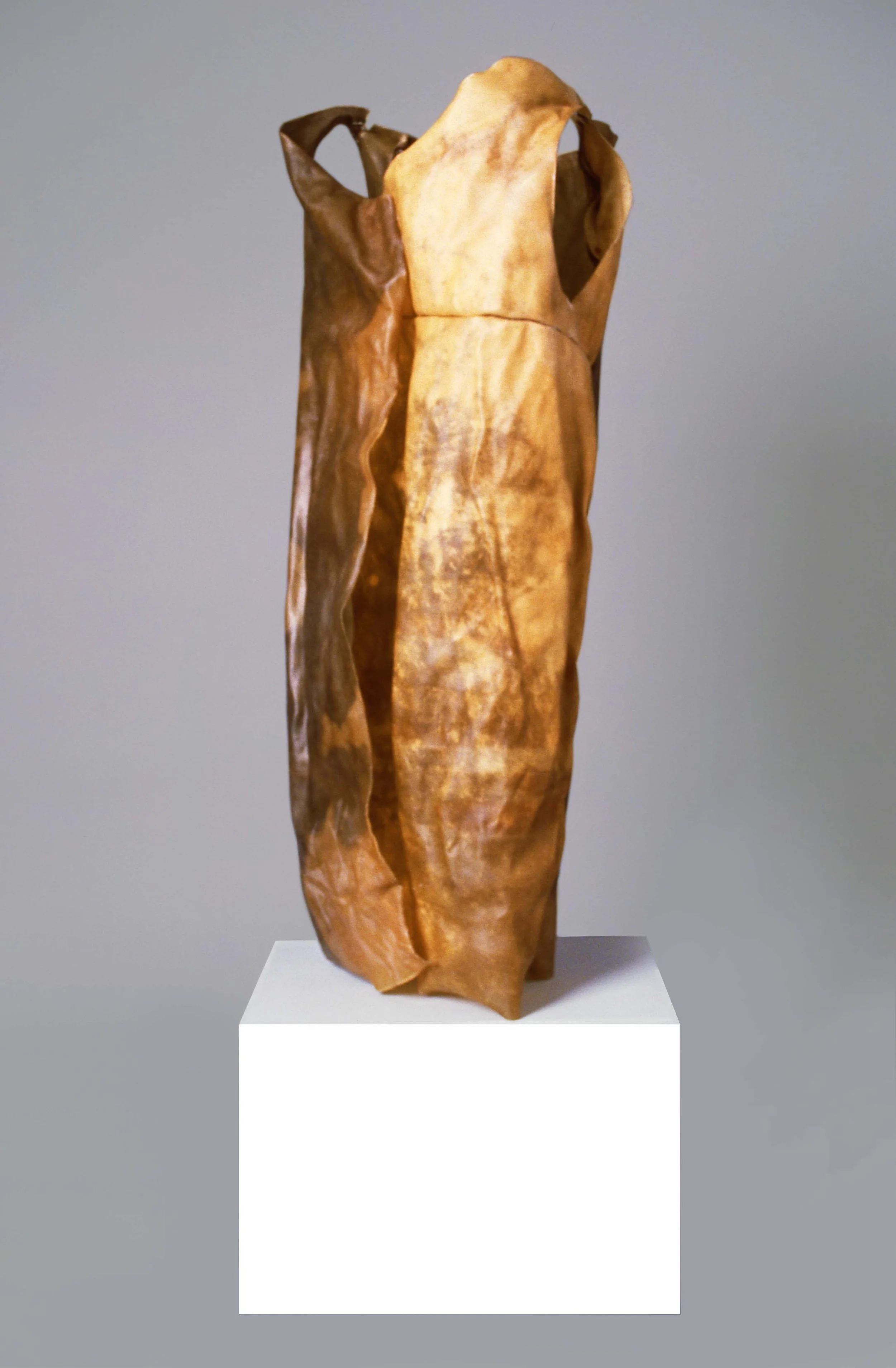 A sculpture of a woman wearing a long, flowing dress, displayed on a white pedestal against a neutral background.