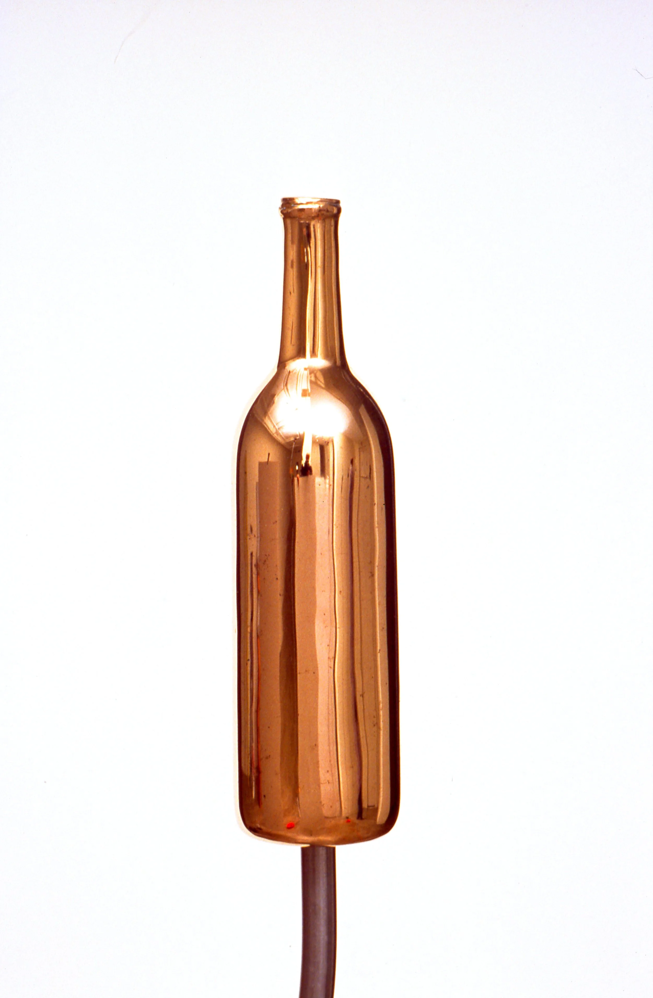 A close-up of a metallic copper-colored object on a white background, resembling a glass ampoule or a decorative bottle.