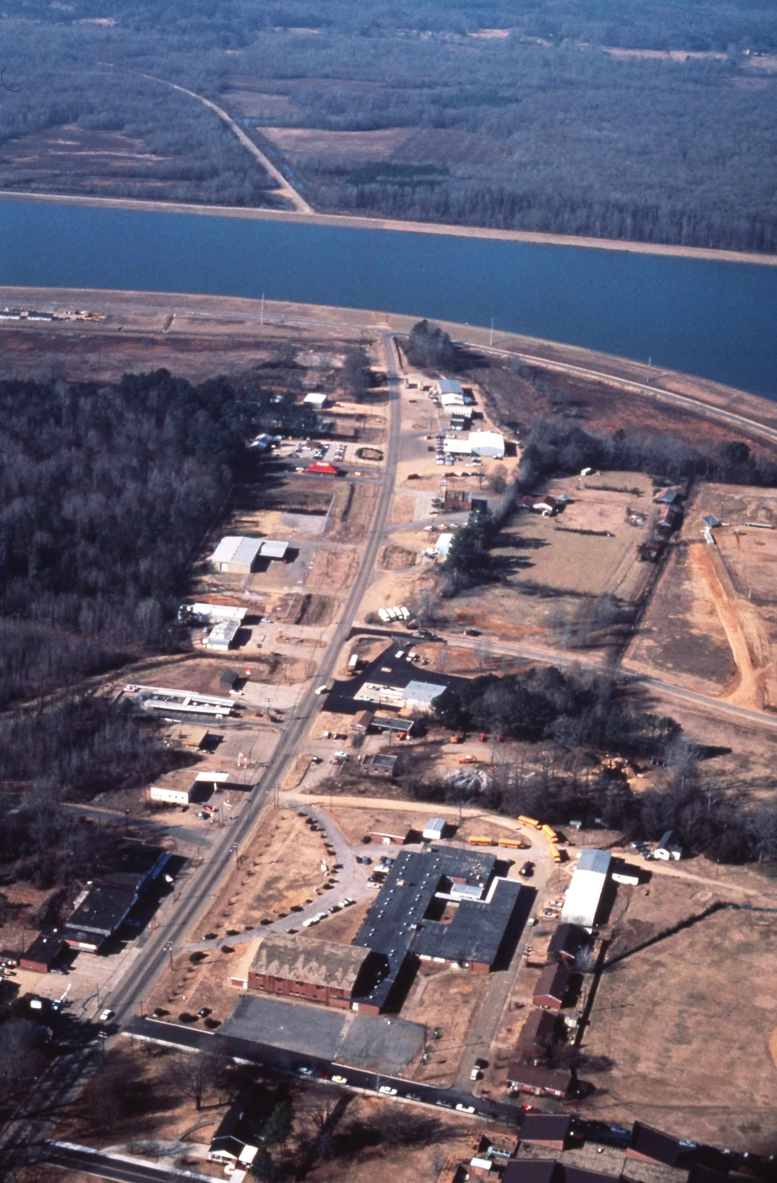 Aerial view of a small town with buildings, roads, a large river, and surrounding wooded and agricultural areas.