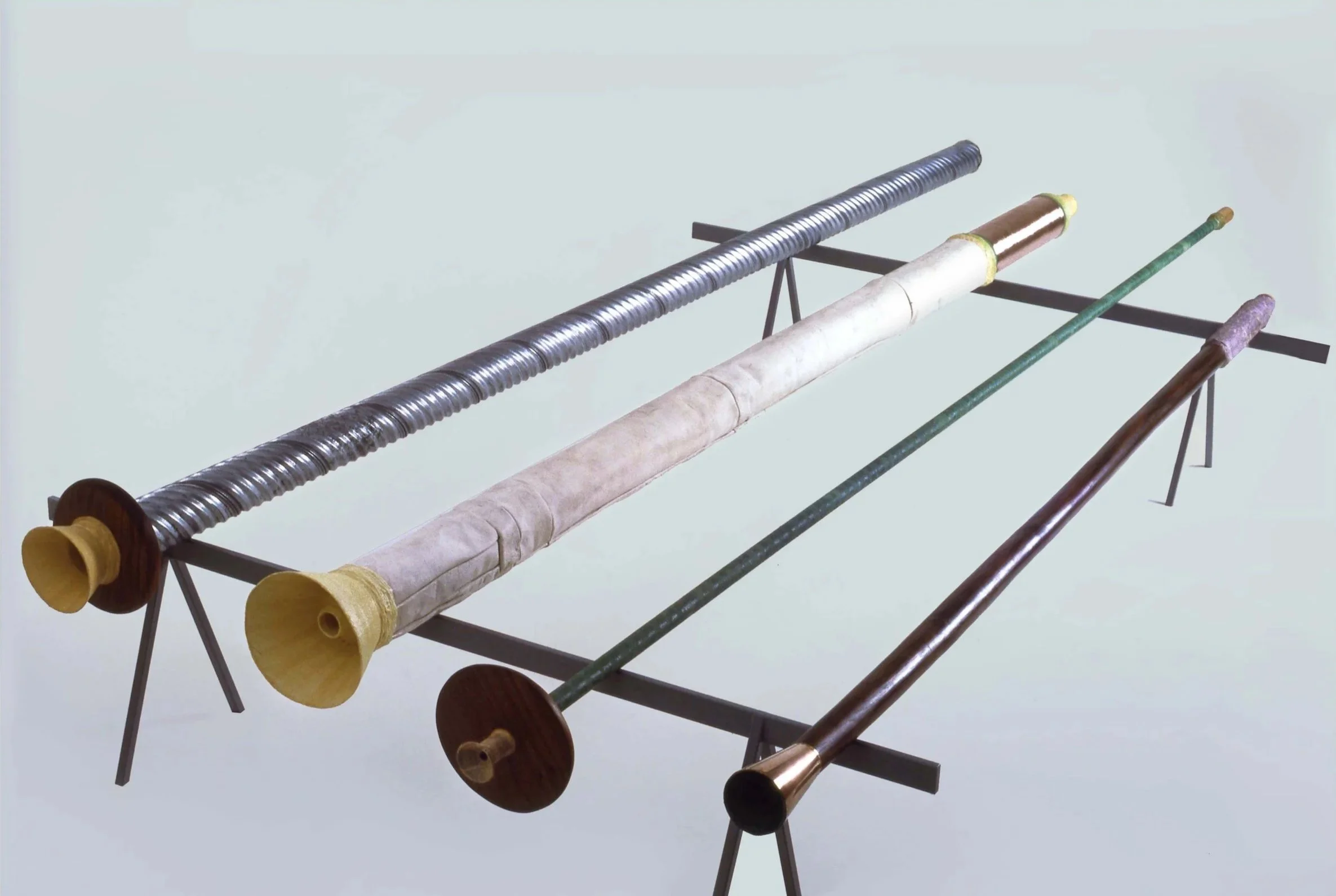 Four musical didgeridoos with different lengths and designs resting on a metal stand.