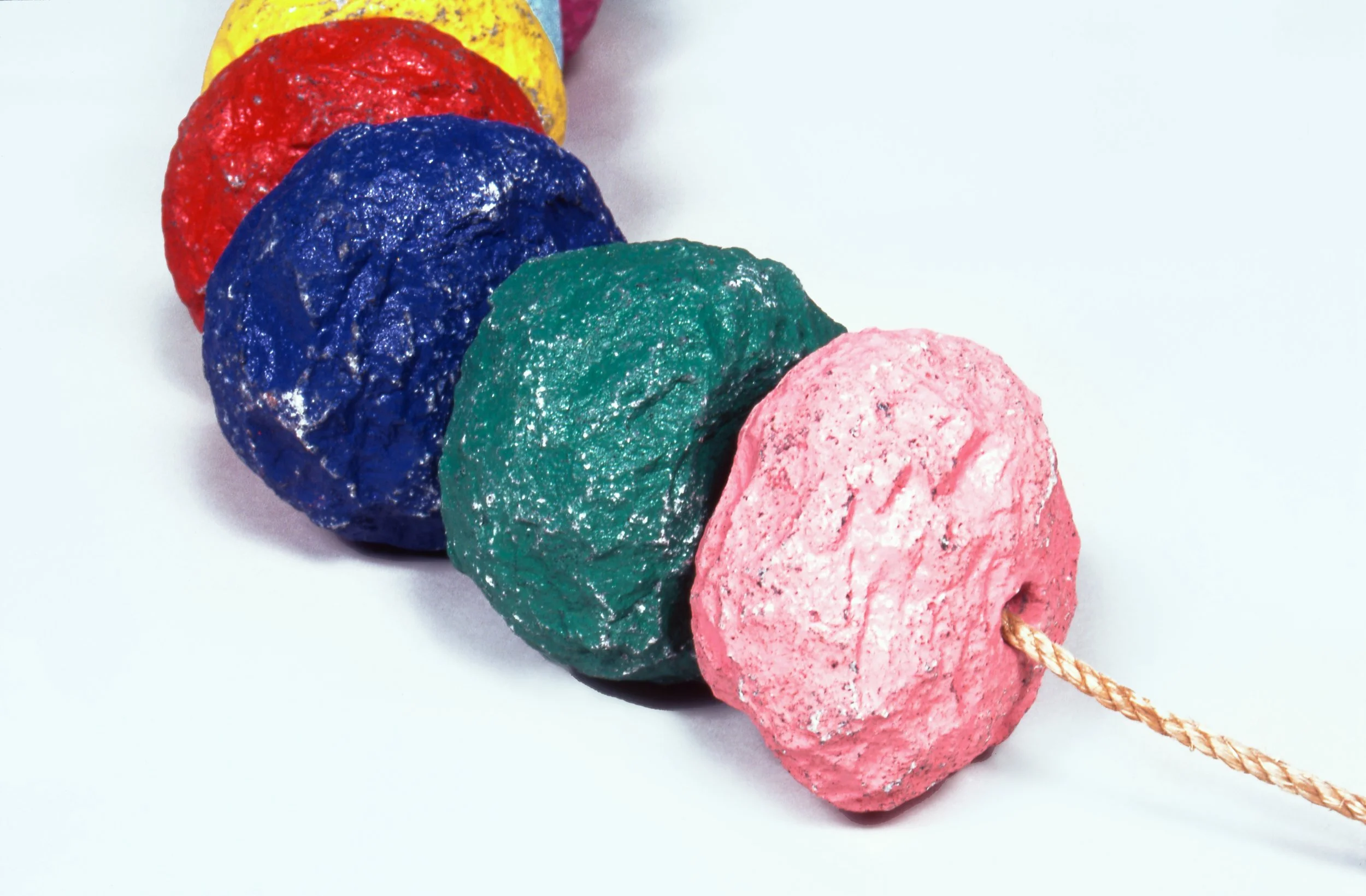Colorful rocks stacked in a line with a pink rock attached to a string against a plain white background.