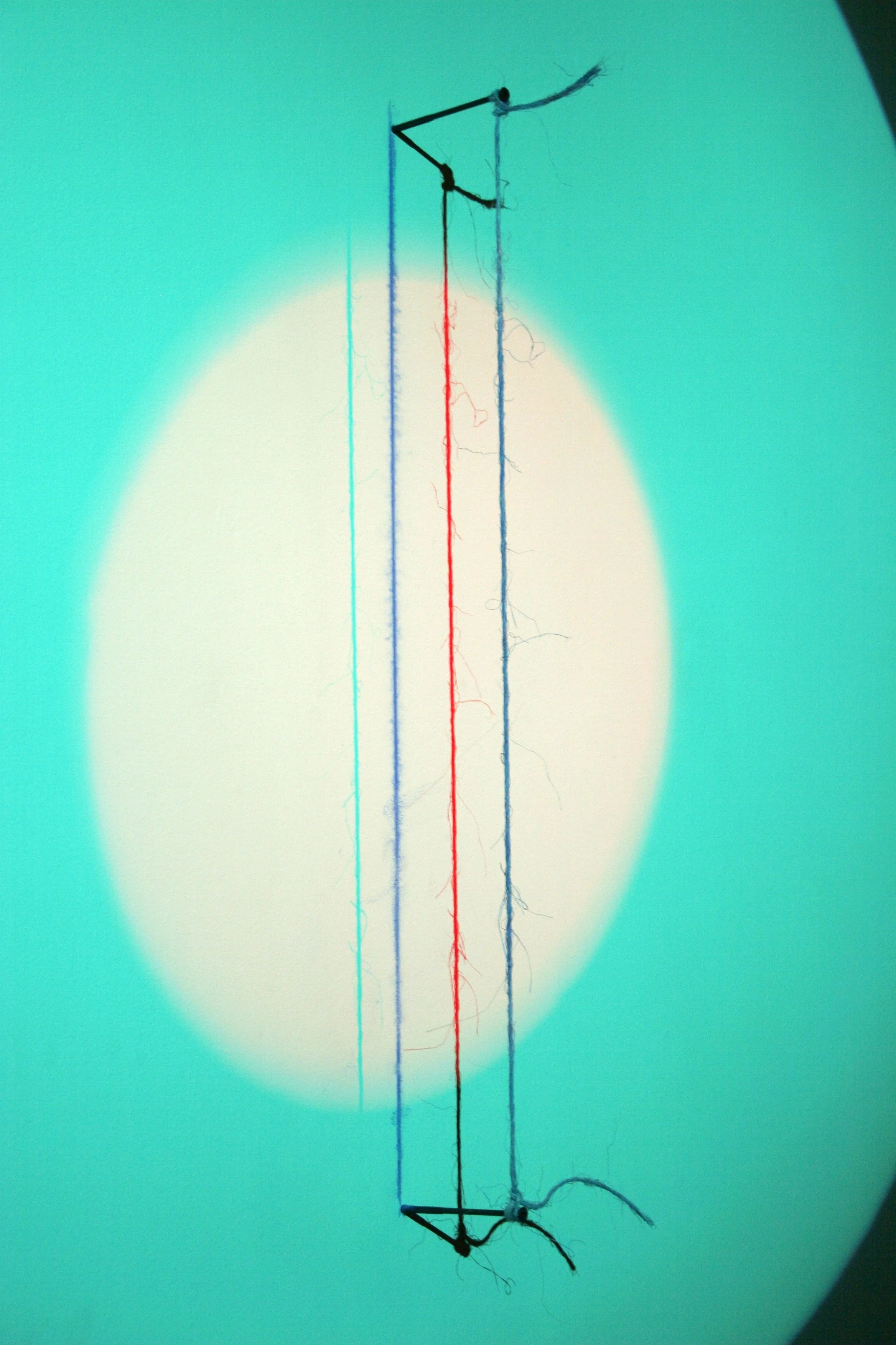 Close-up of a thin, upright electric wire with three colored wires (blue, red, and green) attached, cast on a bright, teal background.
