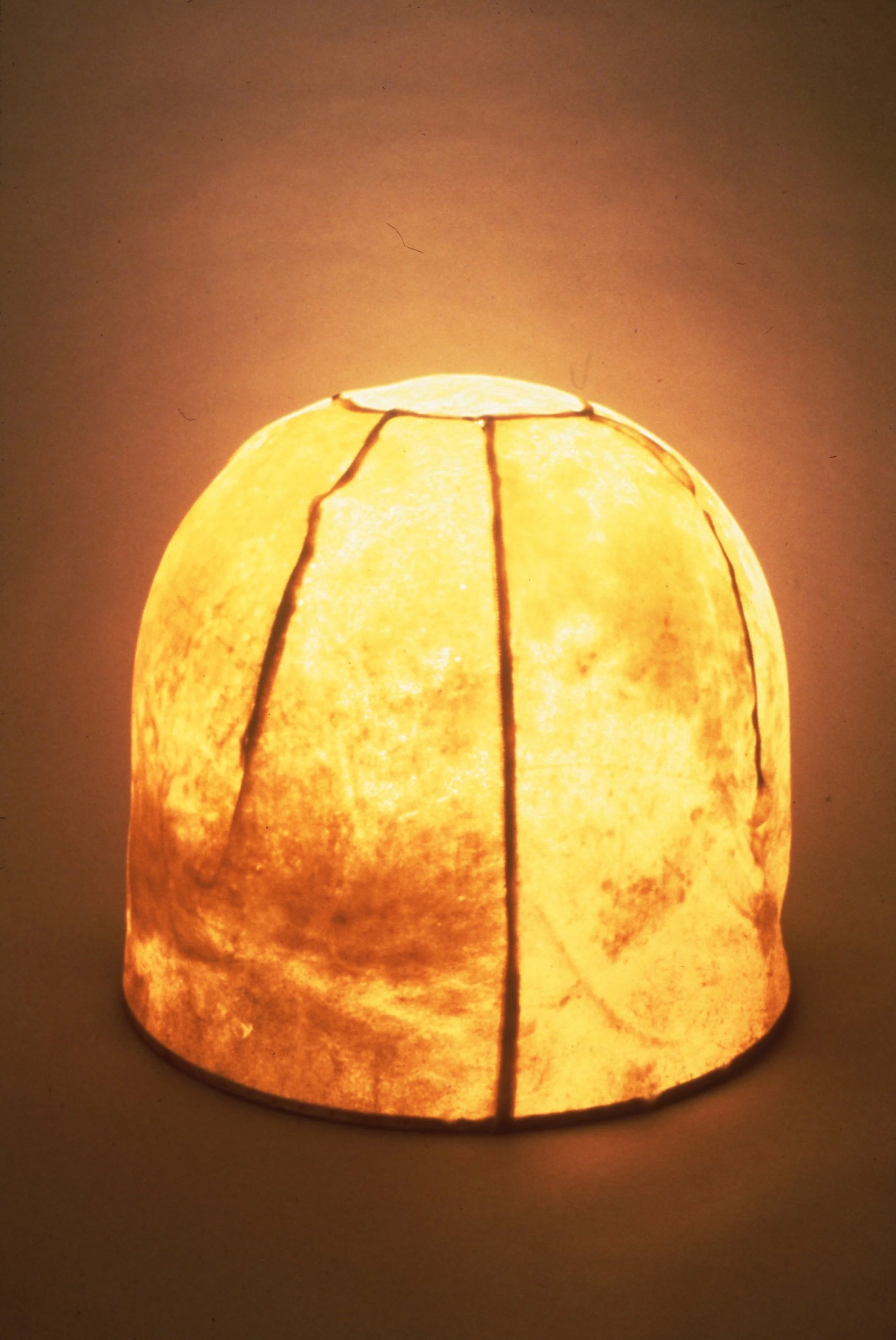 A glowing paper lantern with a textured, marbled surface and dark vertical seams.