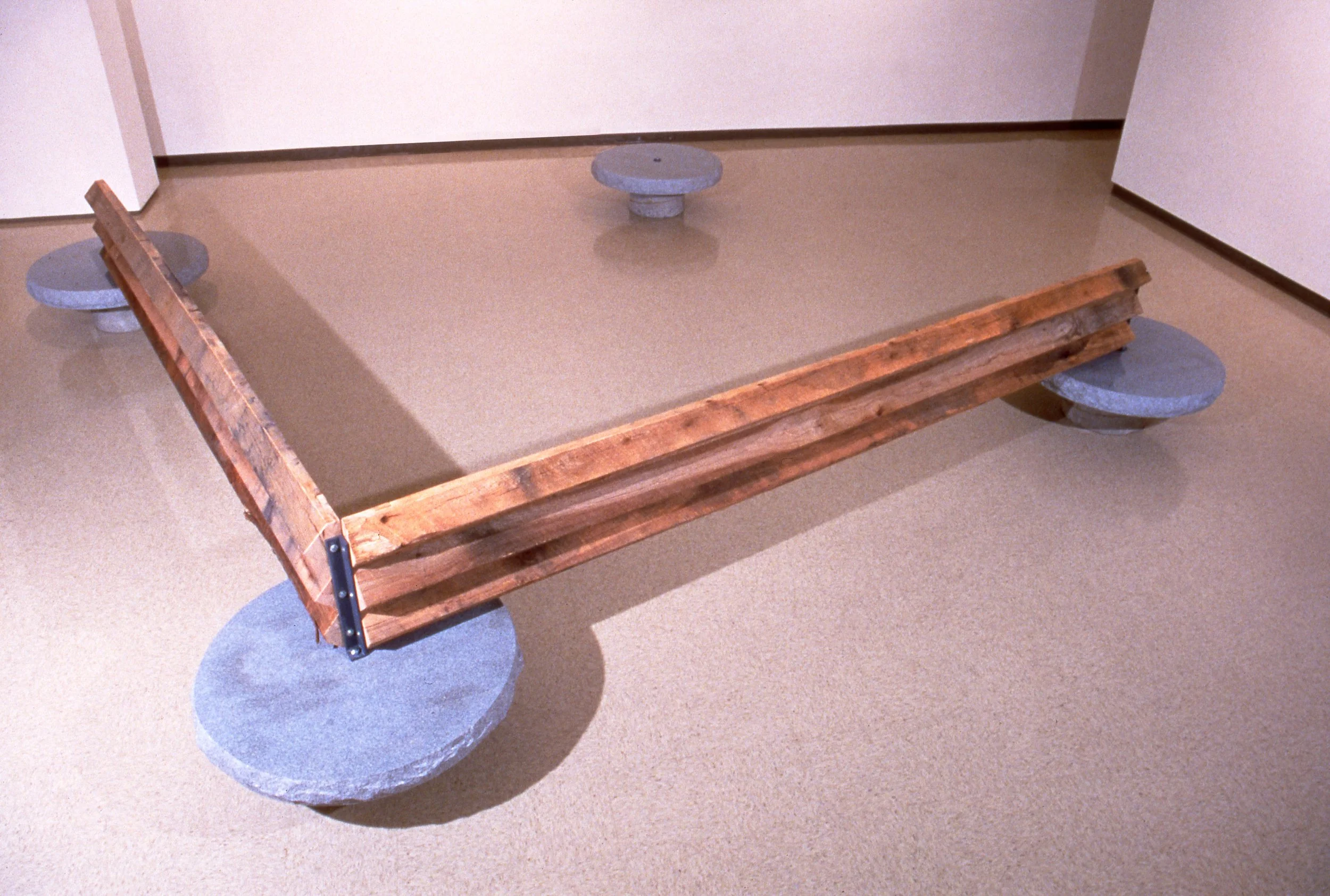 A wooden bench with stone supports on a beige carpeted floor.