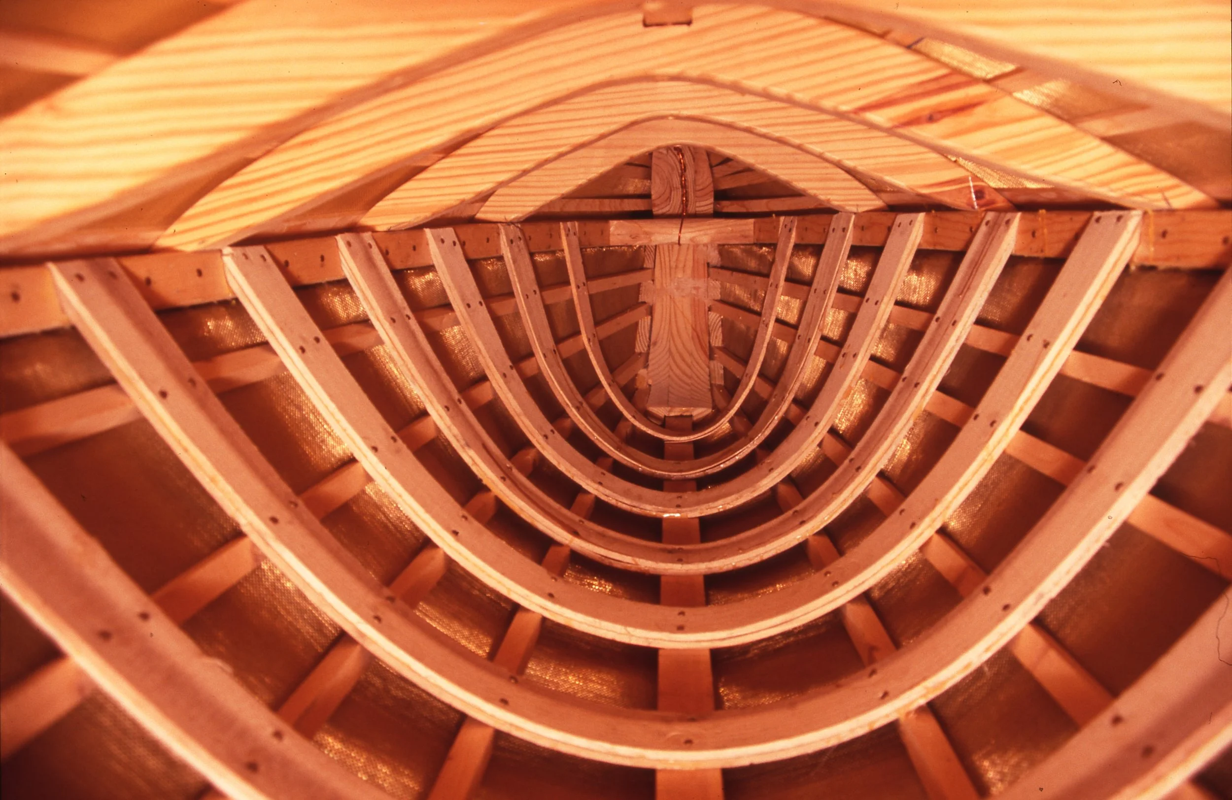Inside view of a wooden boat under construction, showing the curved framework and gunwales.