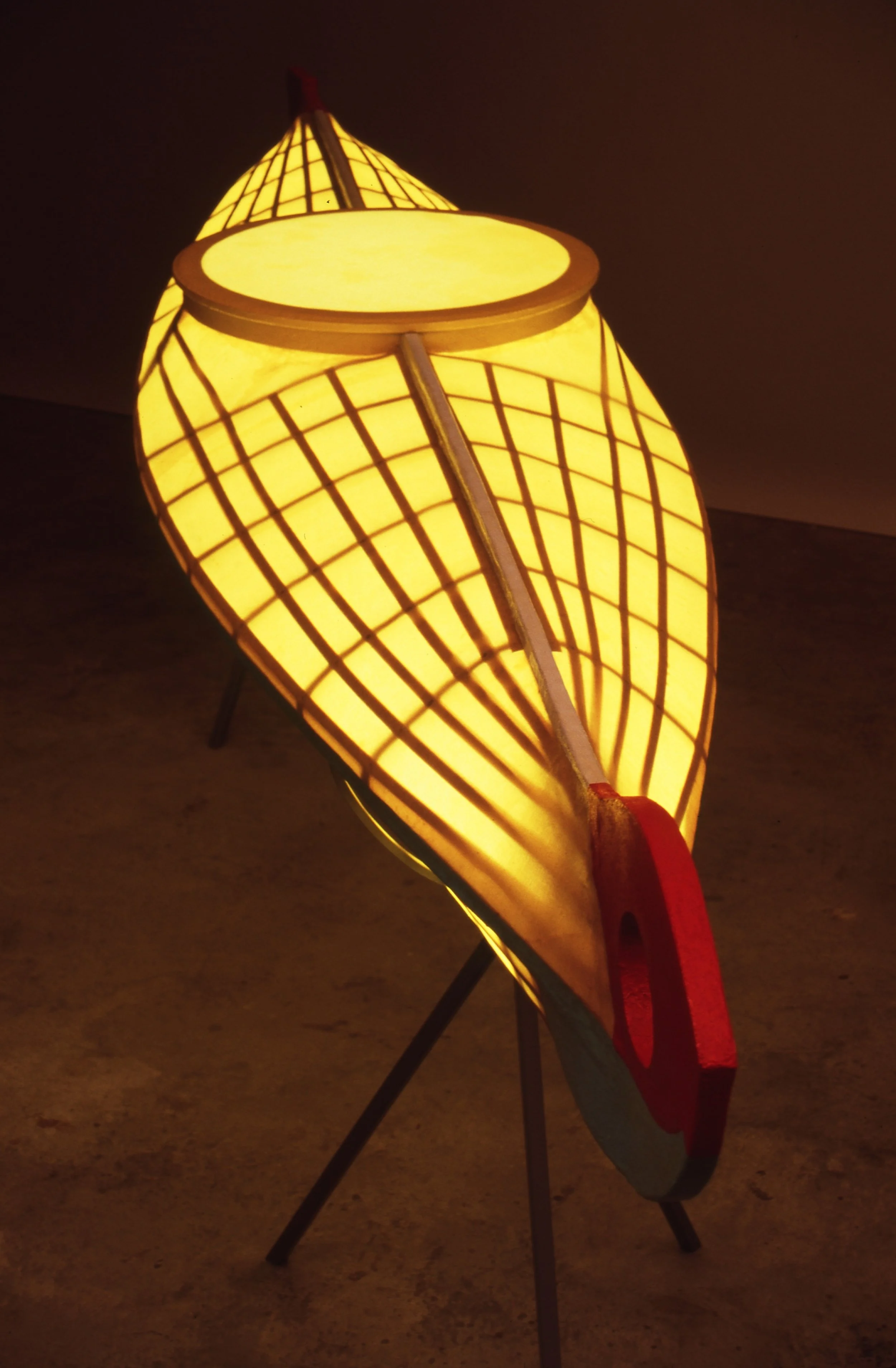 A large illuminated lantern in the shape of a leaf with a circular opening at the top, supported by three black legs.