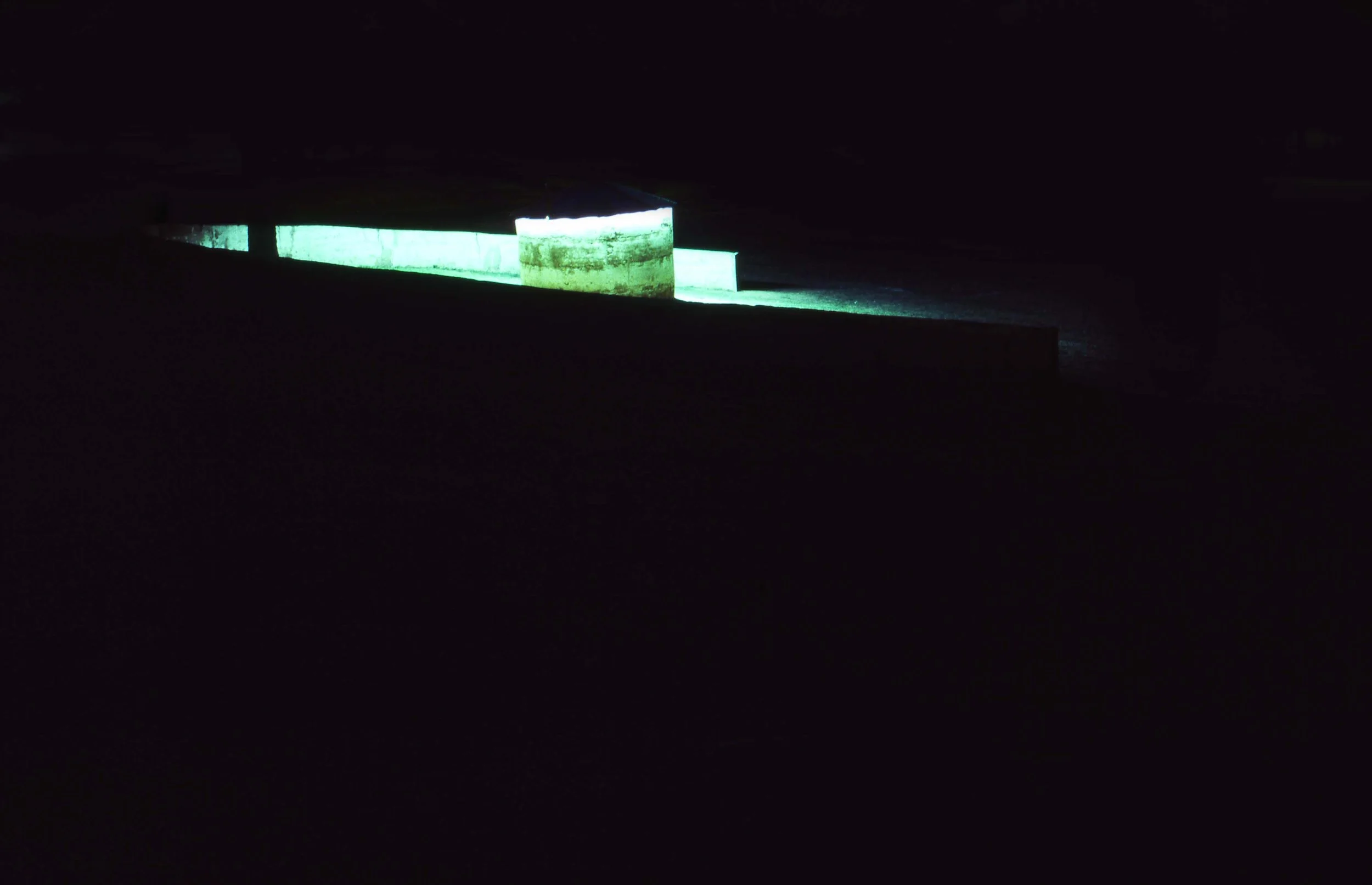 Dark scene with a small glowing green-lit structure in the distance.