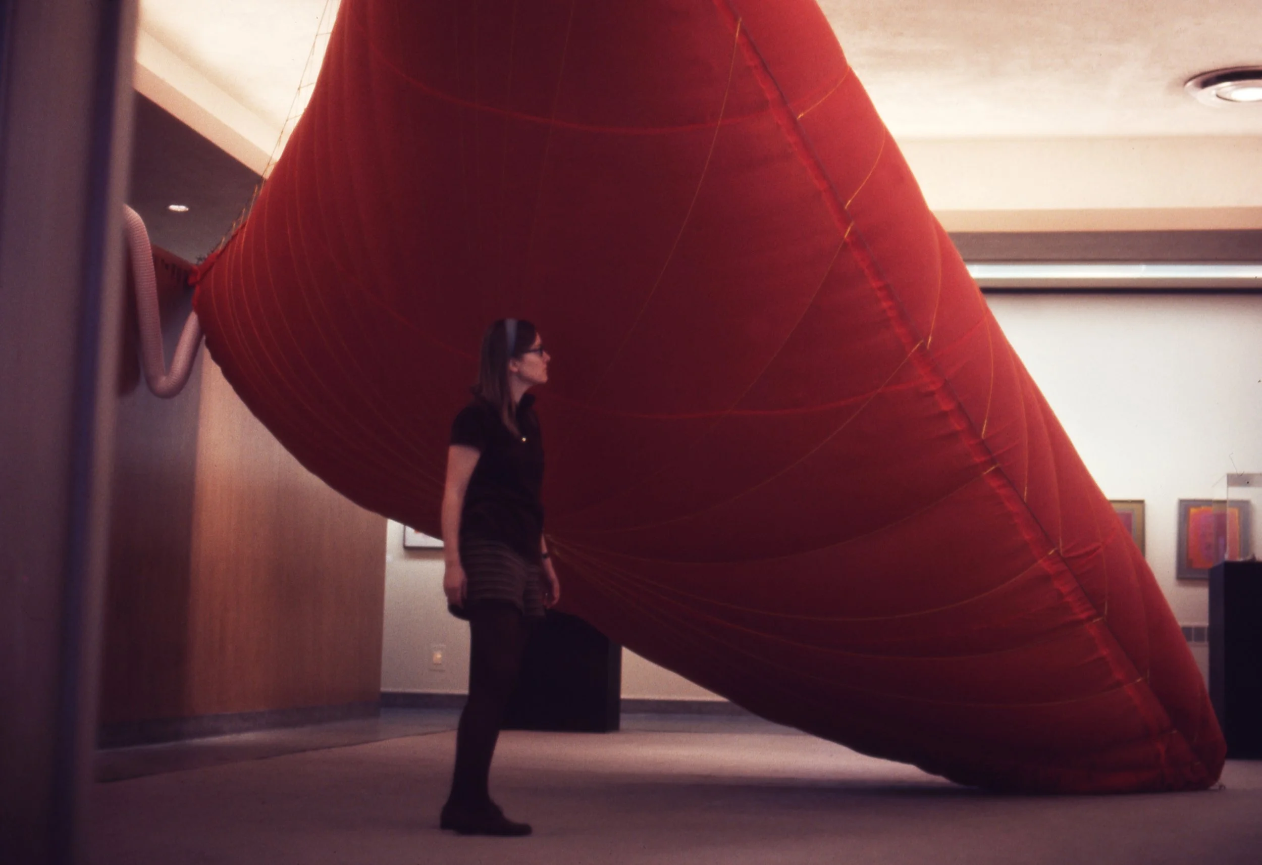 A woman standing next to a large, red, wall-mounted inflatable structure in an indoor setting.