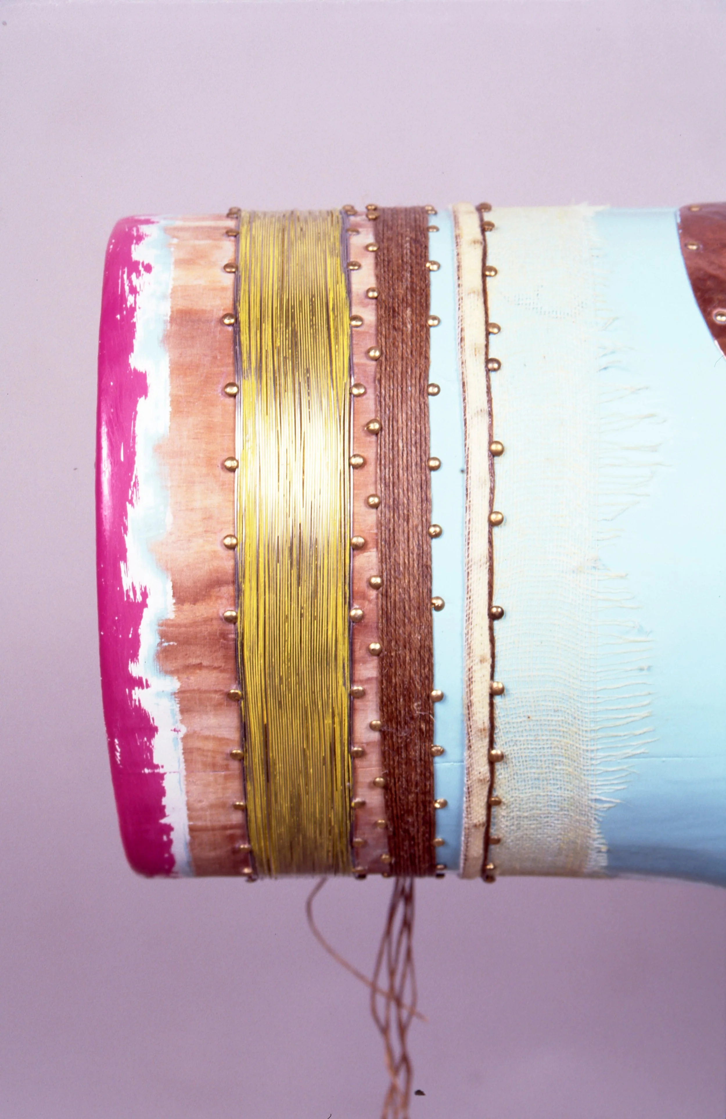 Close-up of a multicolored, decorative cylindrical object with gold pins, including pink, brown, blue, and beige sections, some of which are textured or painted.