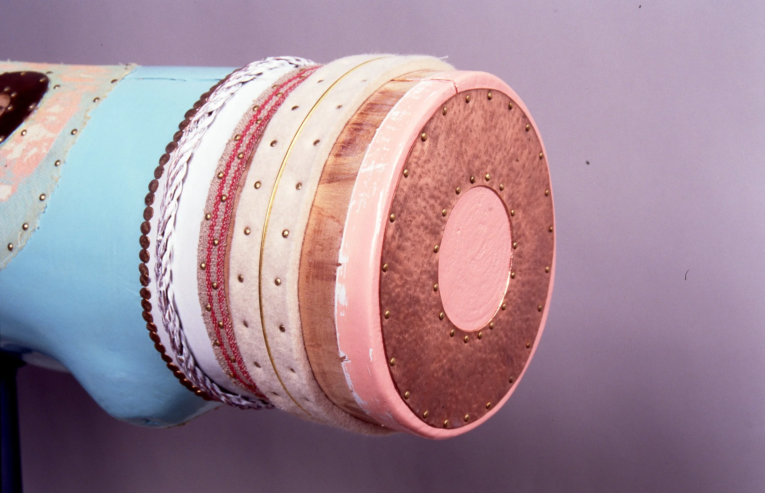 A colorful, layered cake with a variety of textures, including smooth, marbled, and textured surfaces, decorated with small gold beads and pink icing, placed on a purple background.