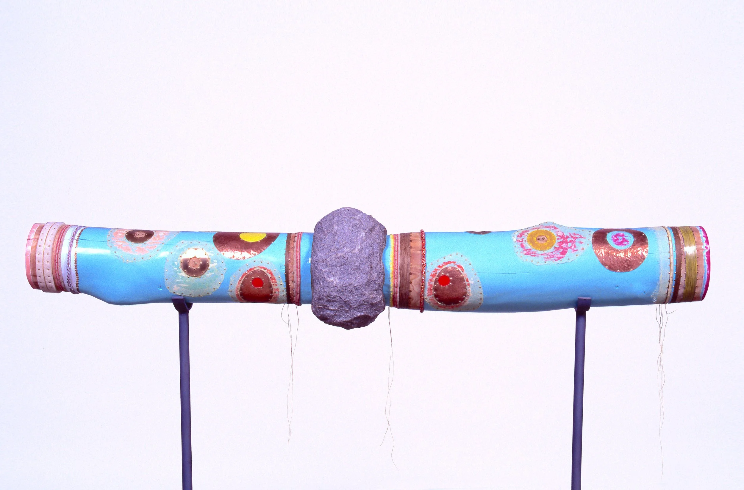 A colorful, decorated telescope with a large gray stone in the middle, mounted on purple stands, set against a plain white background.