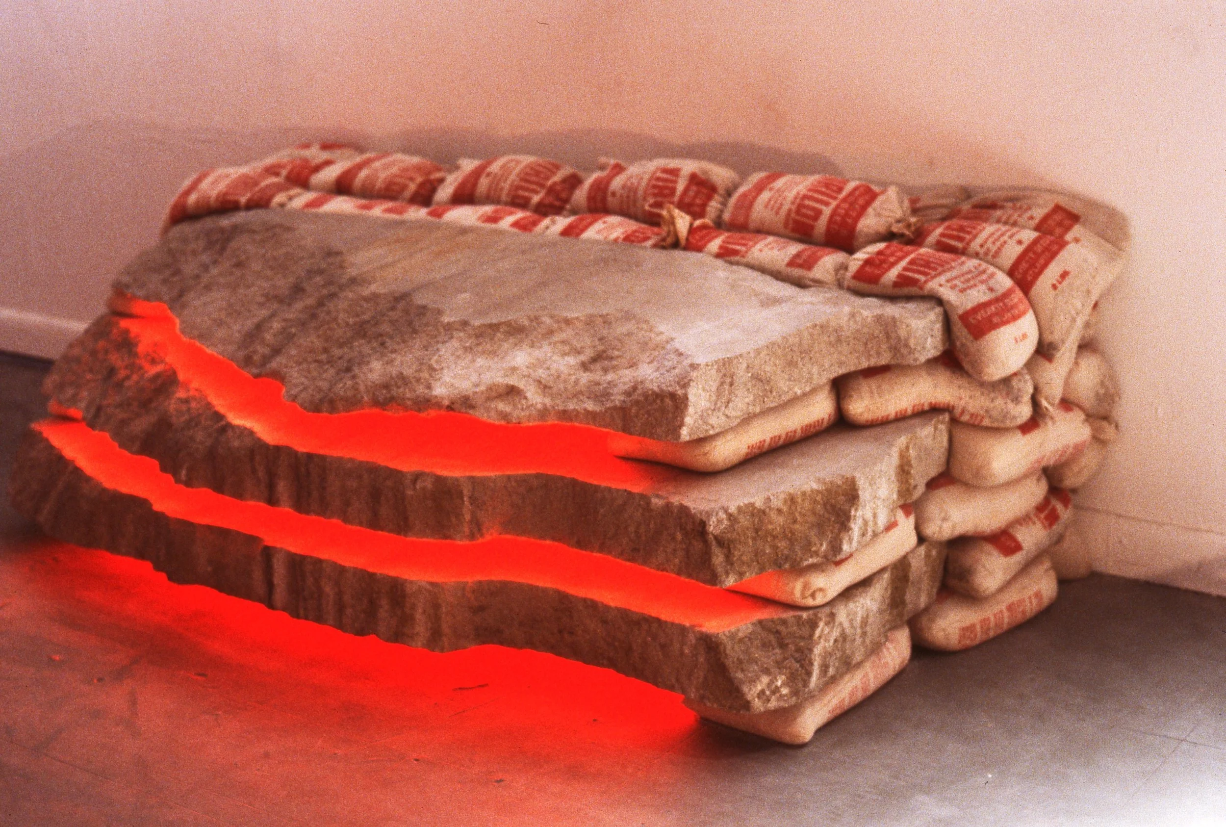 Stack of stone slabs with hidden red lighting underneath, placed on the floor next to a white wall, with cement bags on top.