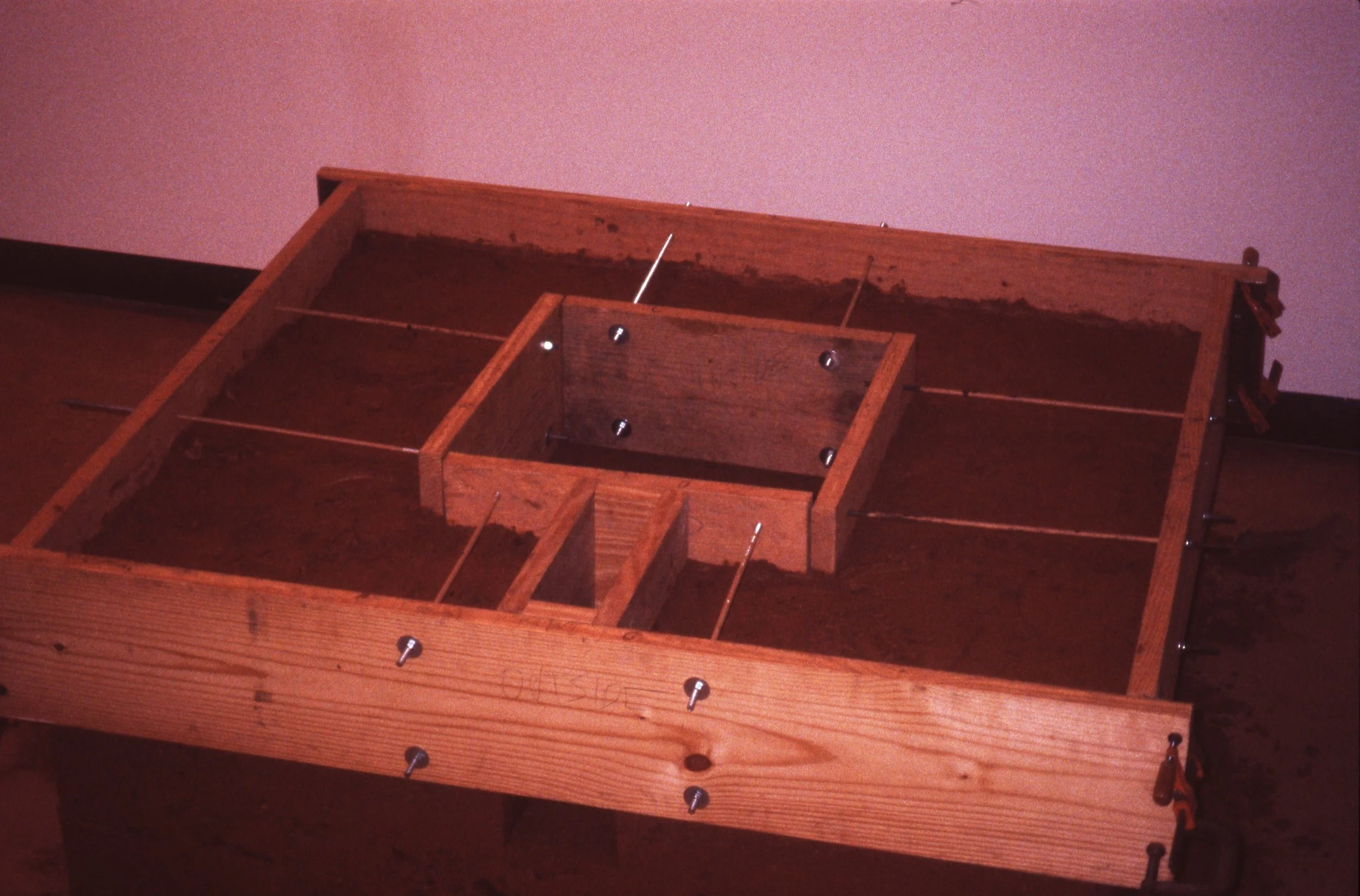 Wooden frame with multiple compartments secured with screws and clamps, set on a wooden surface.