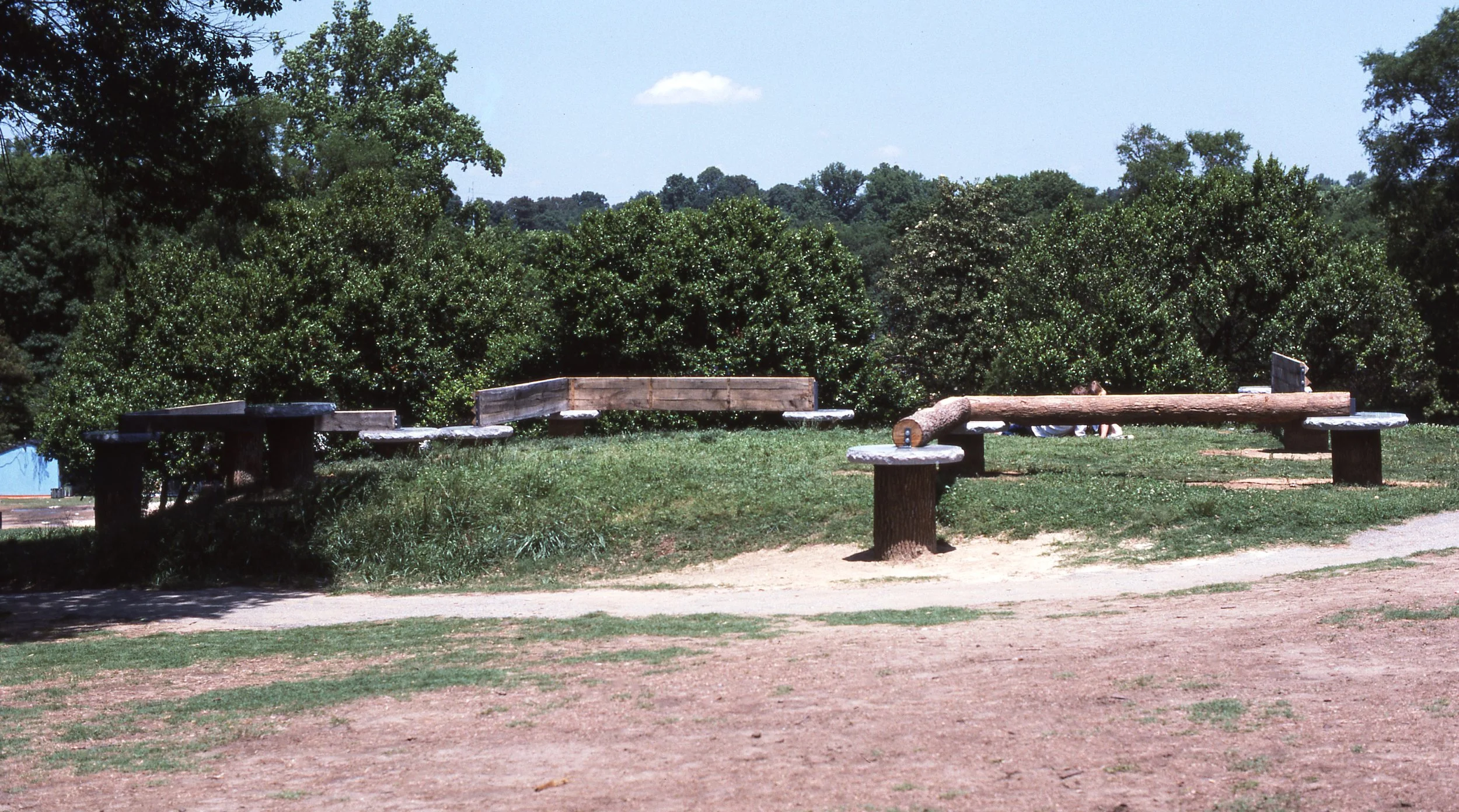 A park scene with wooden benches and green trees in the background under a clear sky.