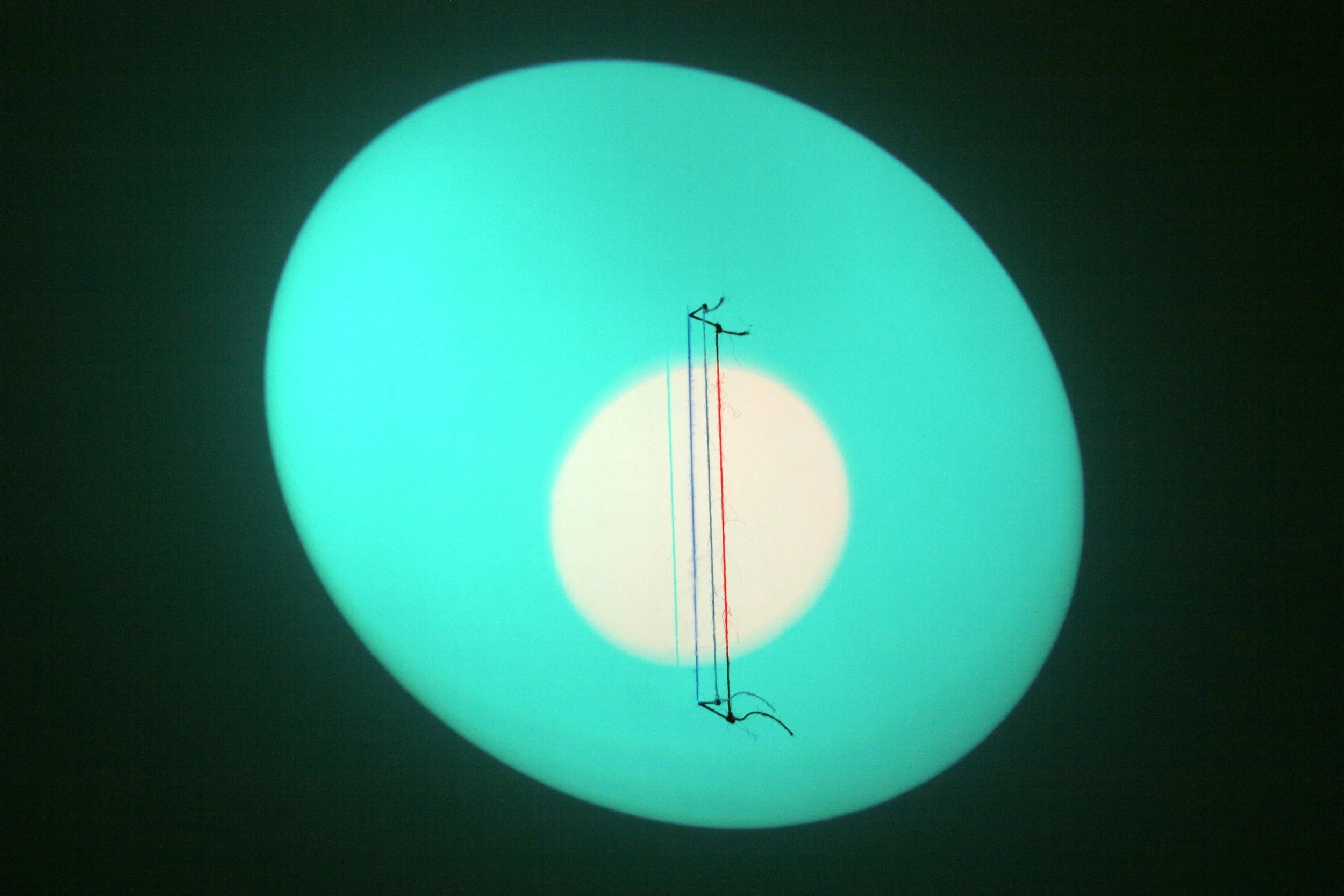 A circular light with green outer glow, with a small white circle in the center, and a small black antenna or wire loop inside the circle.