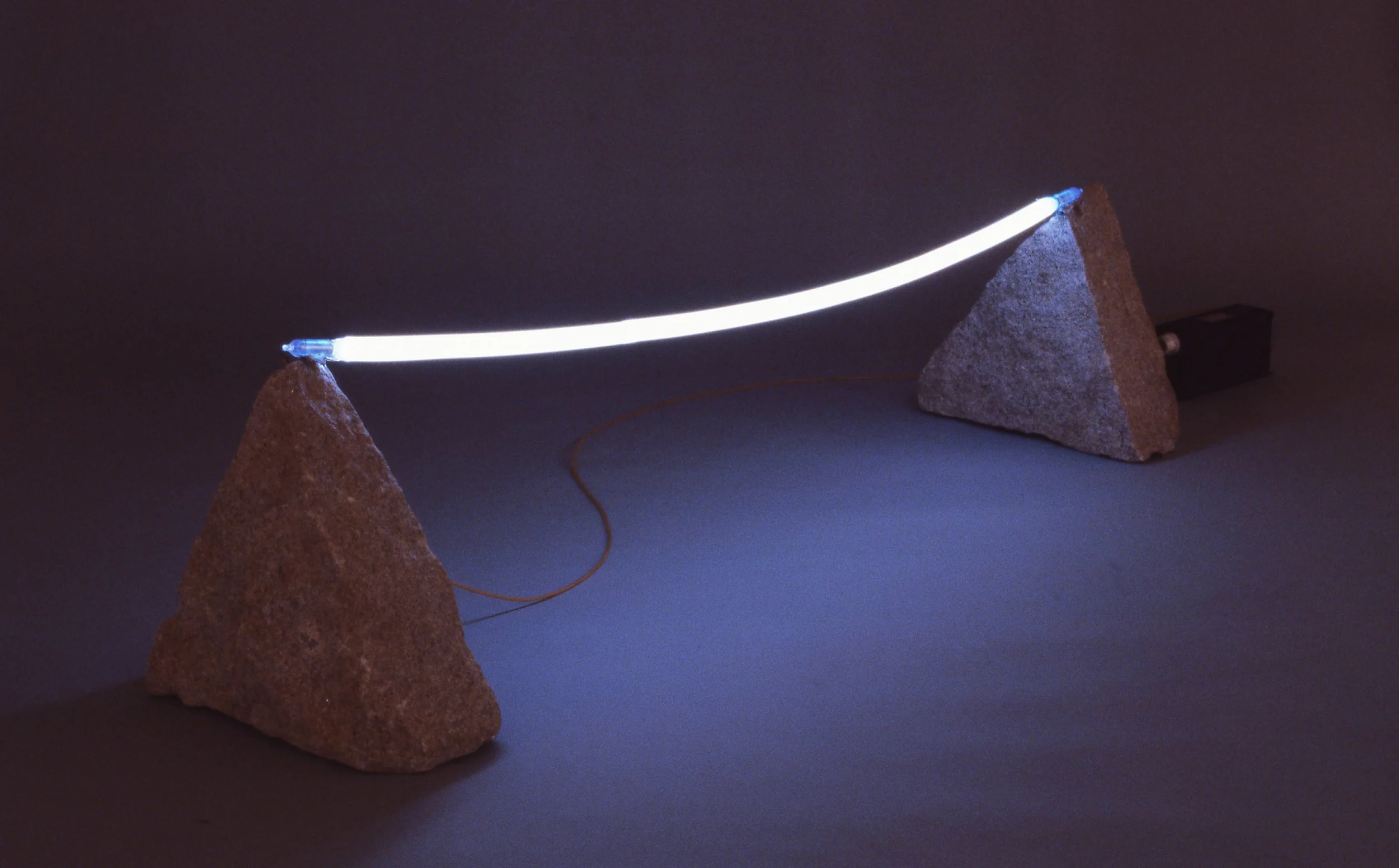 Illuminated LED light strip stretched between two large rocks in a dark environment.