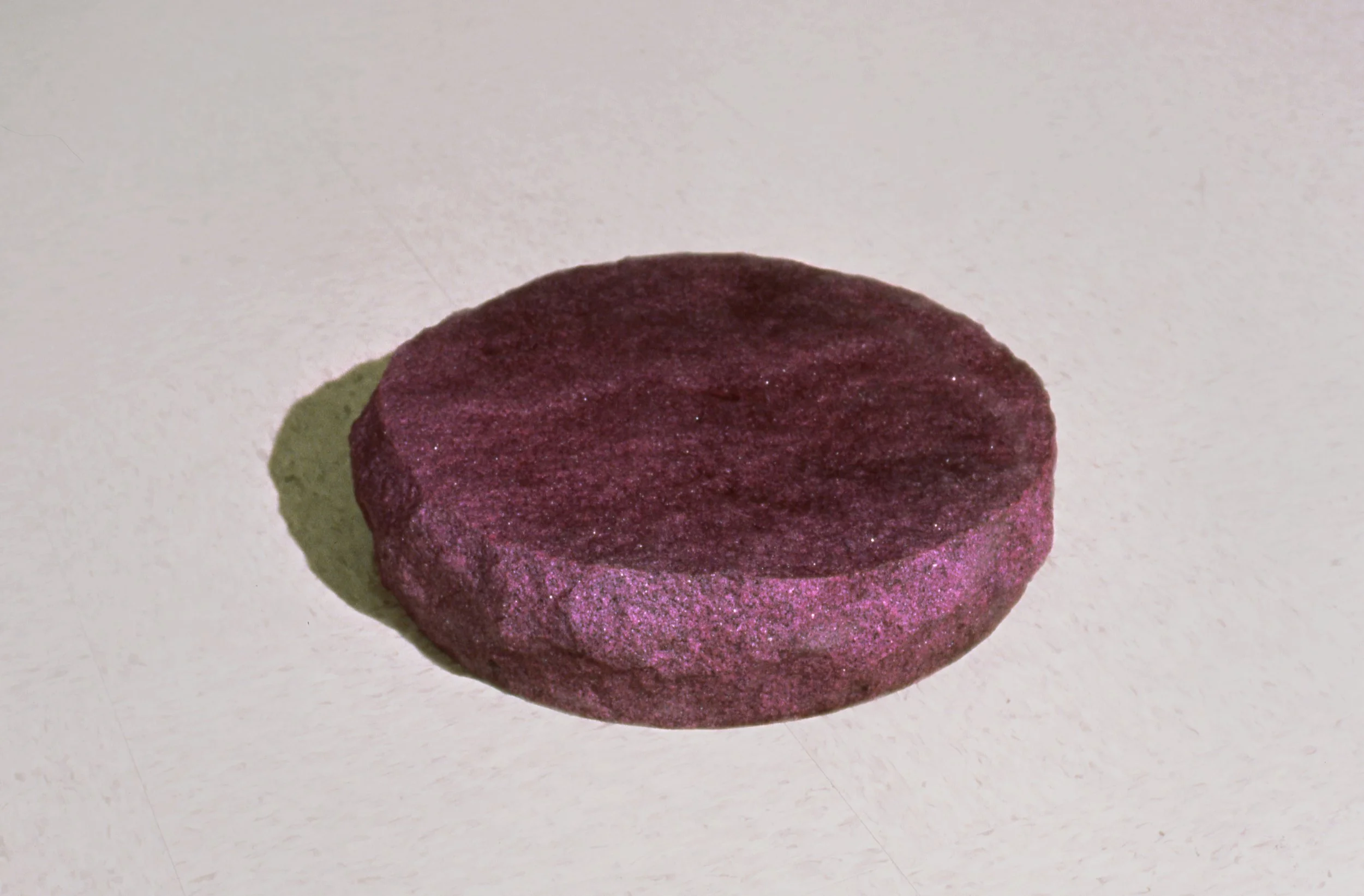 A purple, round, textured disc-shaped object on a white surface.