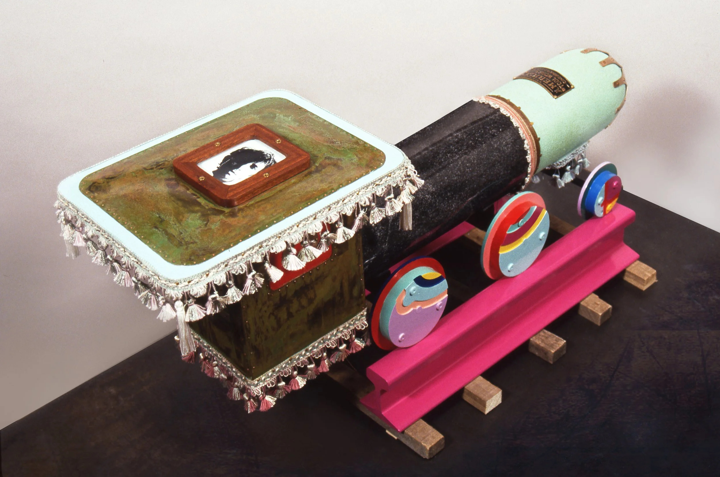 A colorful toy train with a decorated locomotive, painted in shades of pink, black, green, and blue, featuring various circular and geometric designs on its body.