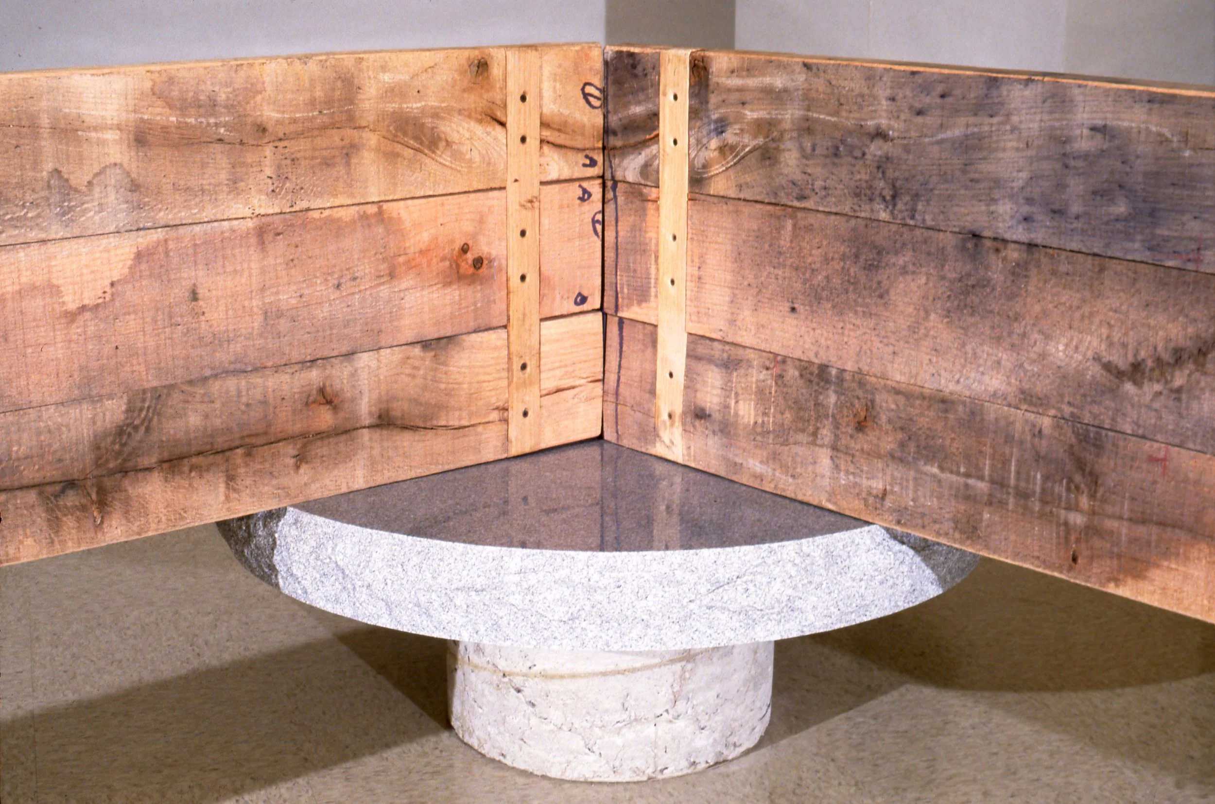 Wooden corner structure with vertical supports and a granite base, likely part of a construction or architectural project.