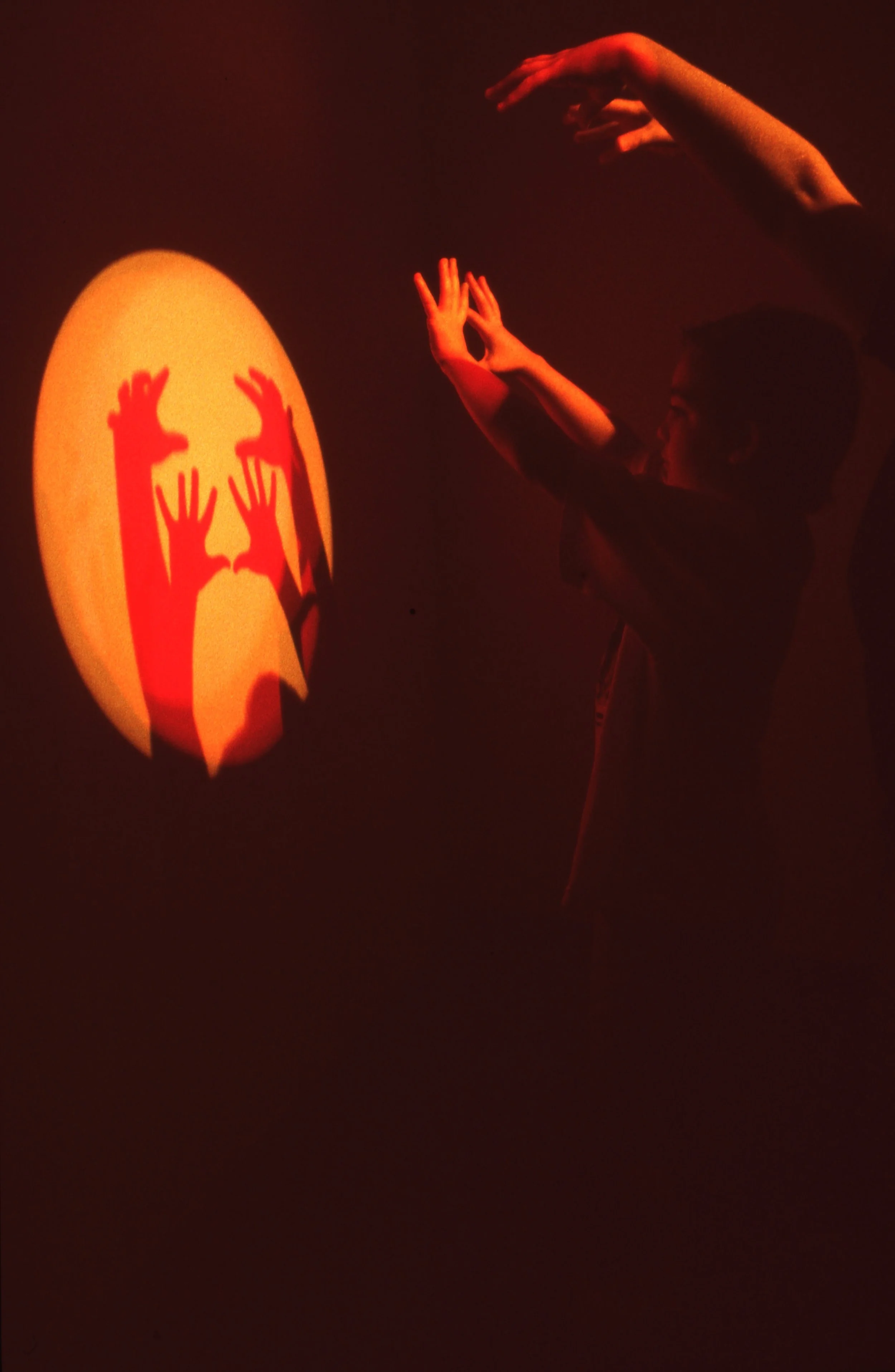 A person creates shadow puppets on a wall using their hands, with the shadow resembling a face with raised hands.