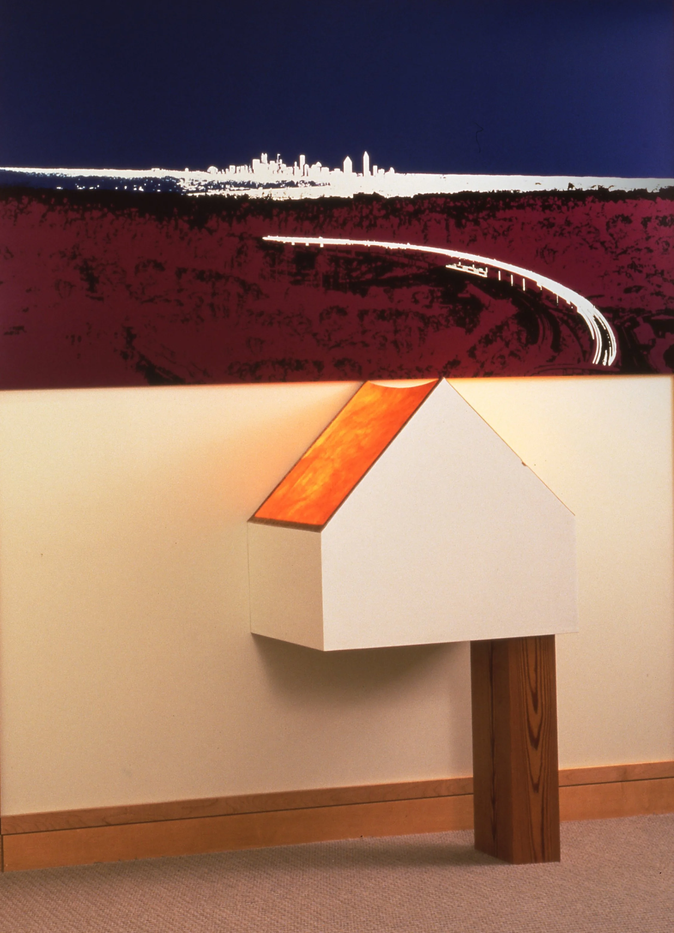 A small white house-shaped object with a wooden base and a peaked roof with a warm-toned surface, mounted on a wall