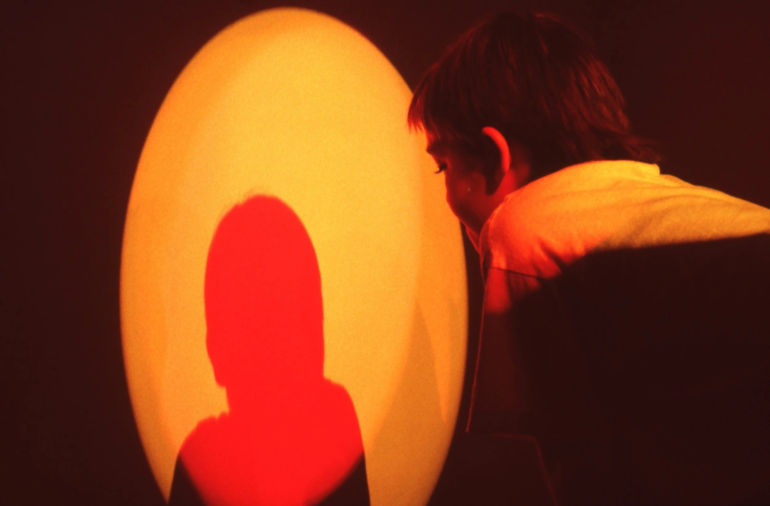 A boy looking at a large, illuminated, oval-shaped screen with a red silhouette of a person's head and shoulders in front of him.