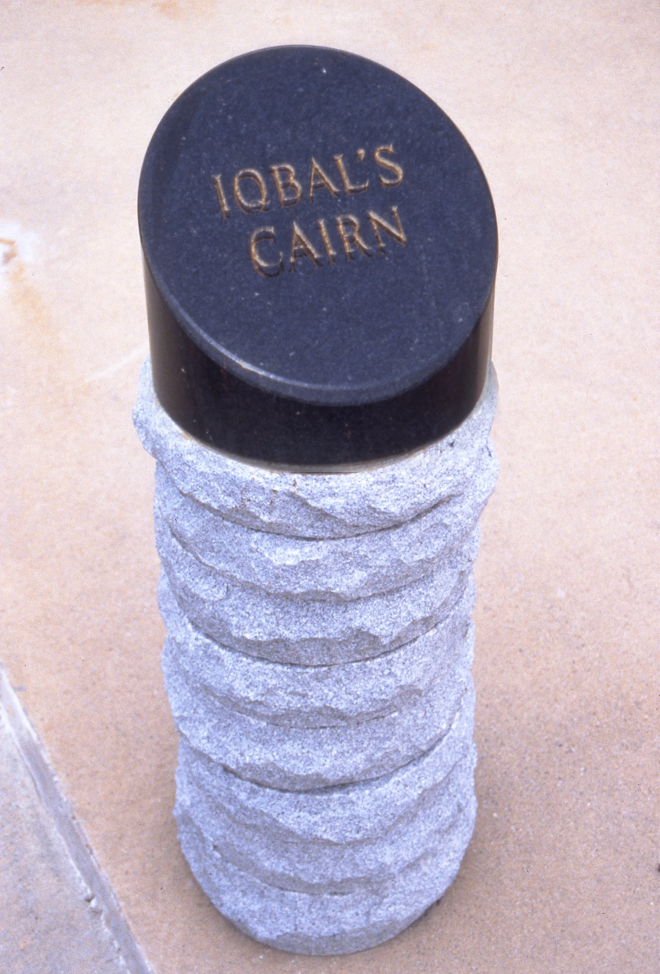 Stack of grey rocks with a black round rock on top that has the words "IQBAL'S GARN" engraved on it.