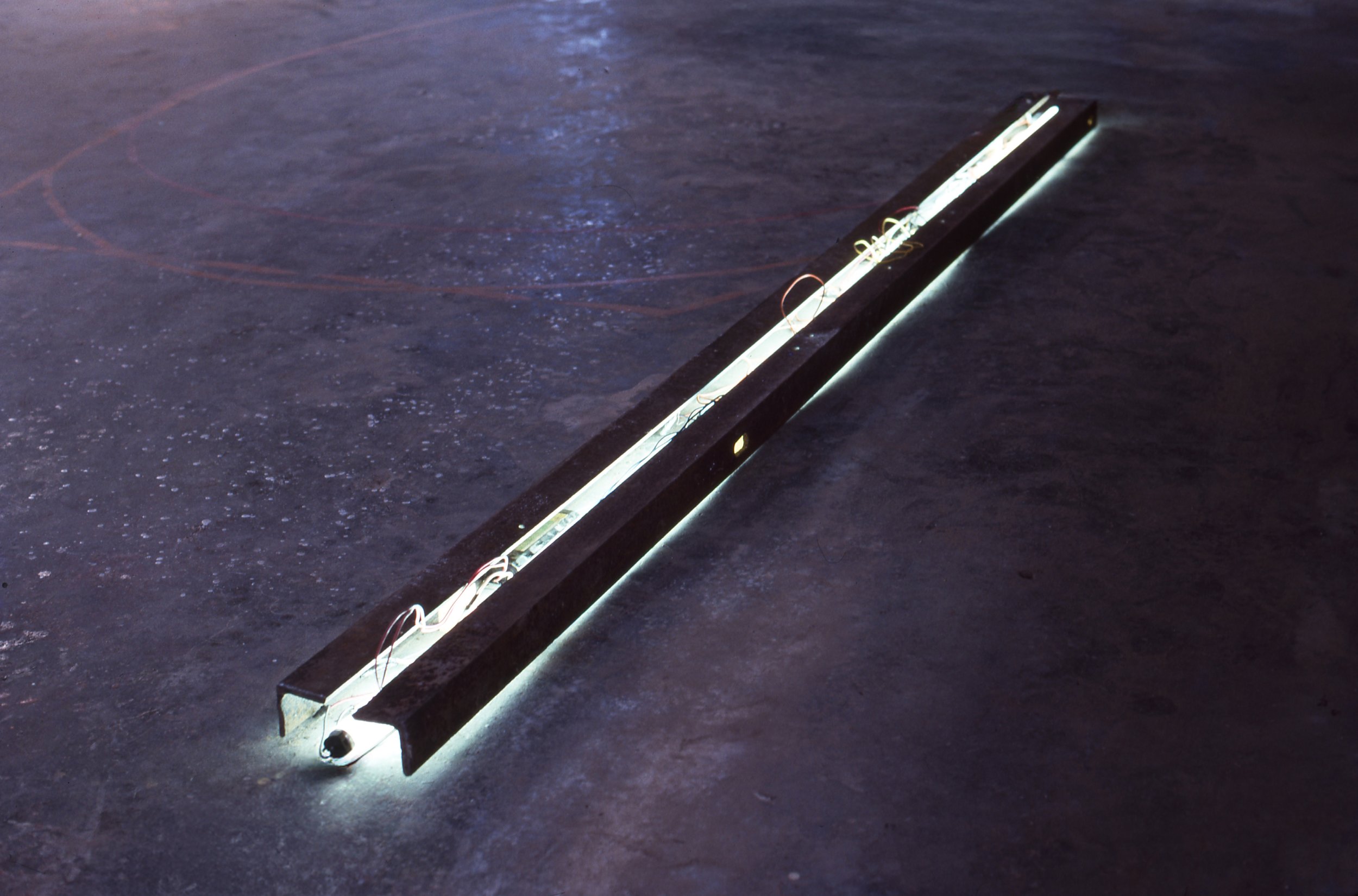 A long, black rectangular LED light strip placed on a dark, textured floor with some light reflections.