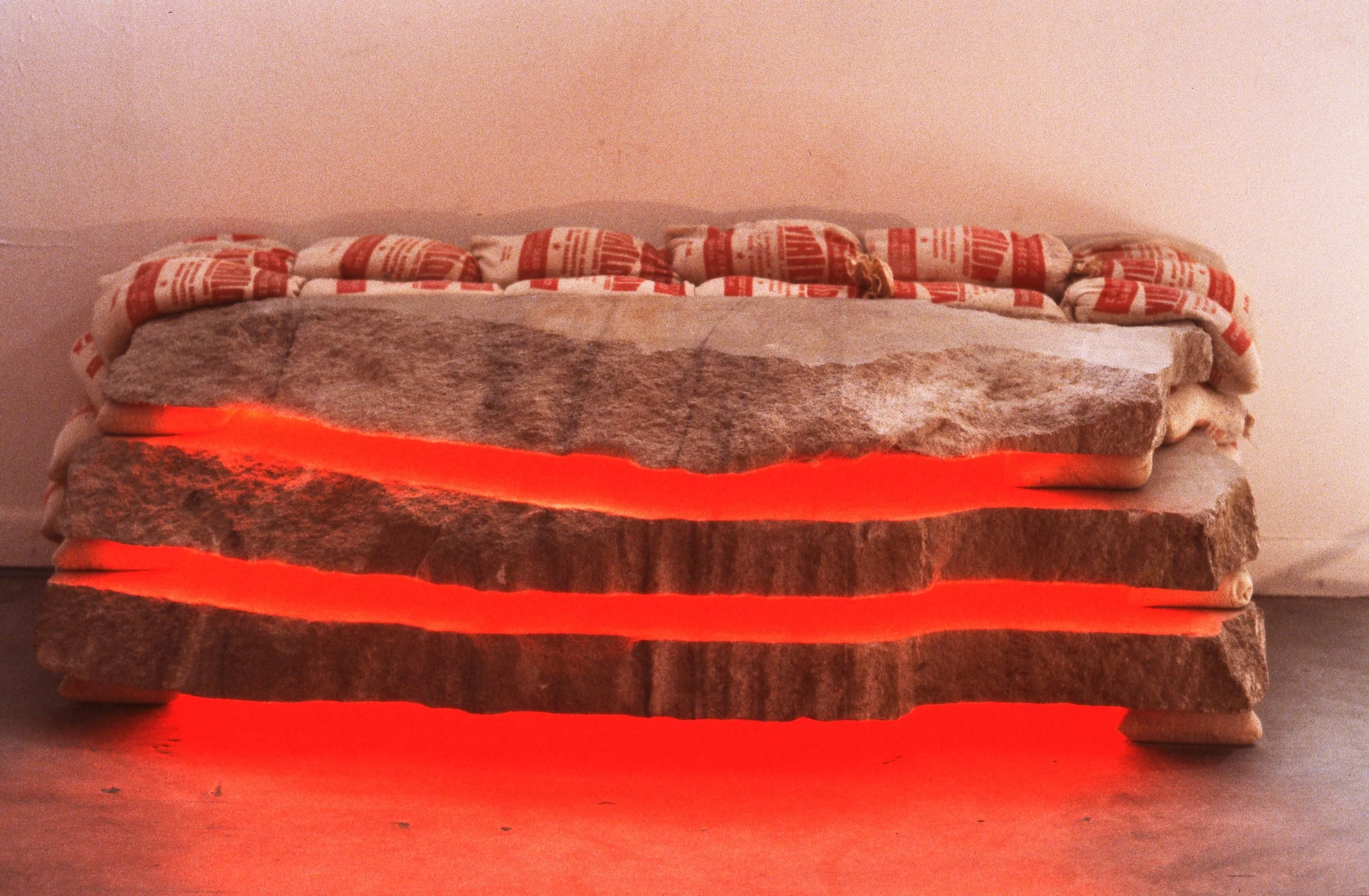 A layered stone sculpture with glowing red light emanating from between the stones, topped with fabric bags.