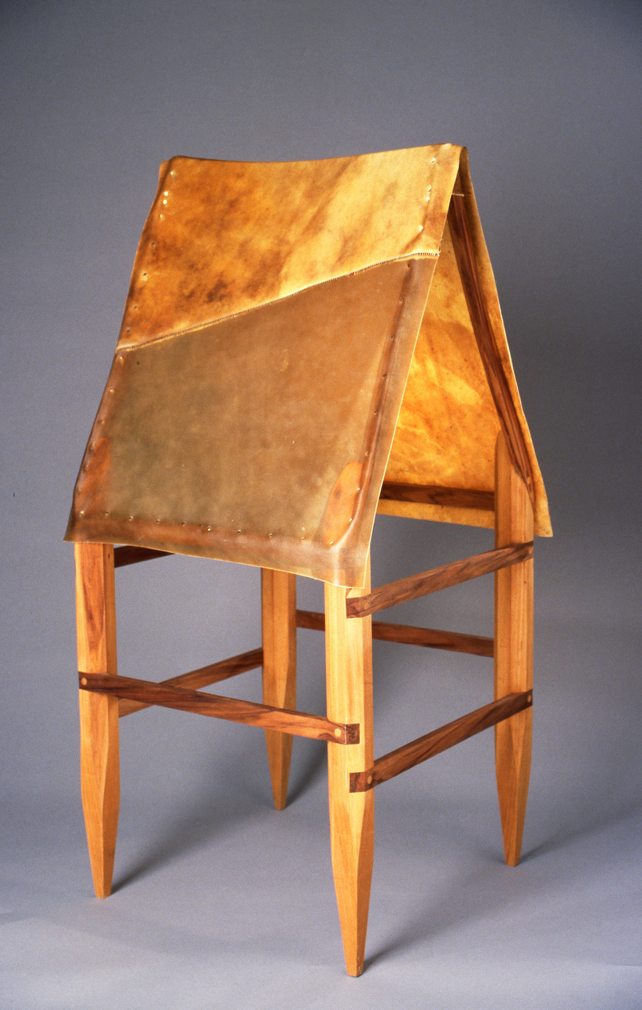 An art piece with a wooden stand and a metallic, slightly curved, two-tone gold and copper-colored top.
