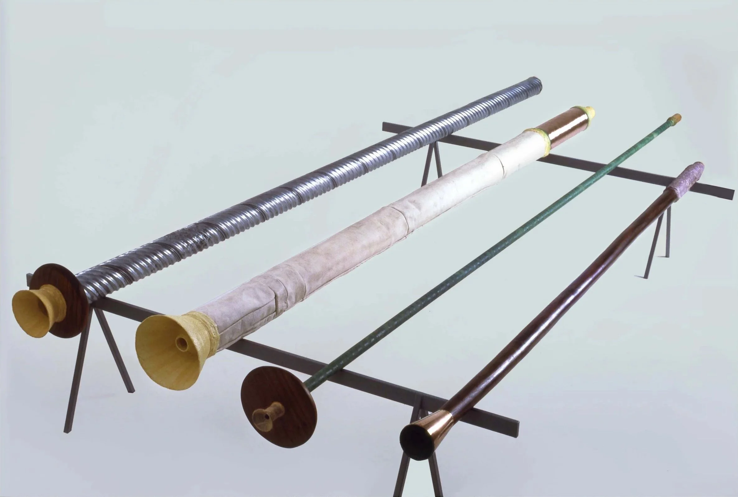 Four long wind instruments placed on a stand, each with a different material and design.