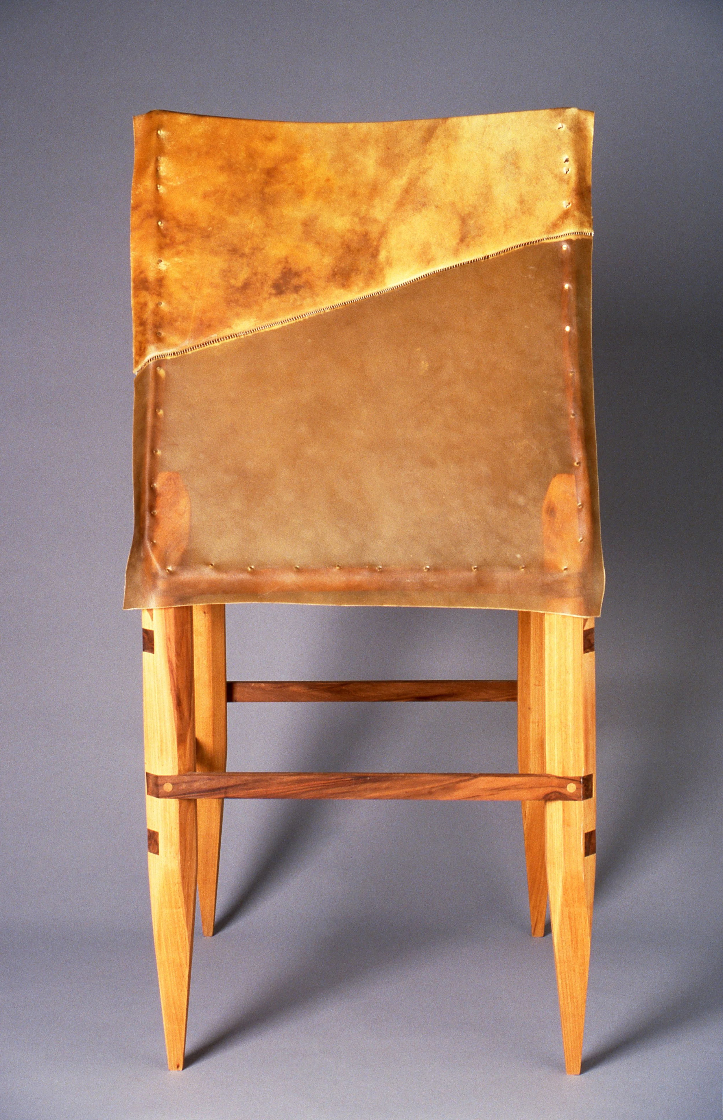 A wooden chair with a high backrest padded in worn, distressed leather.