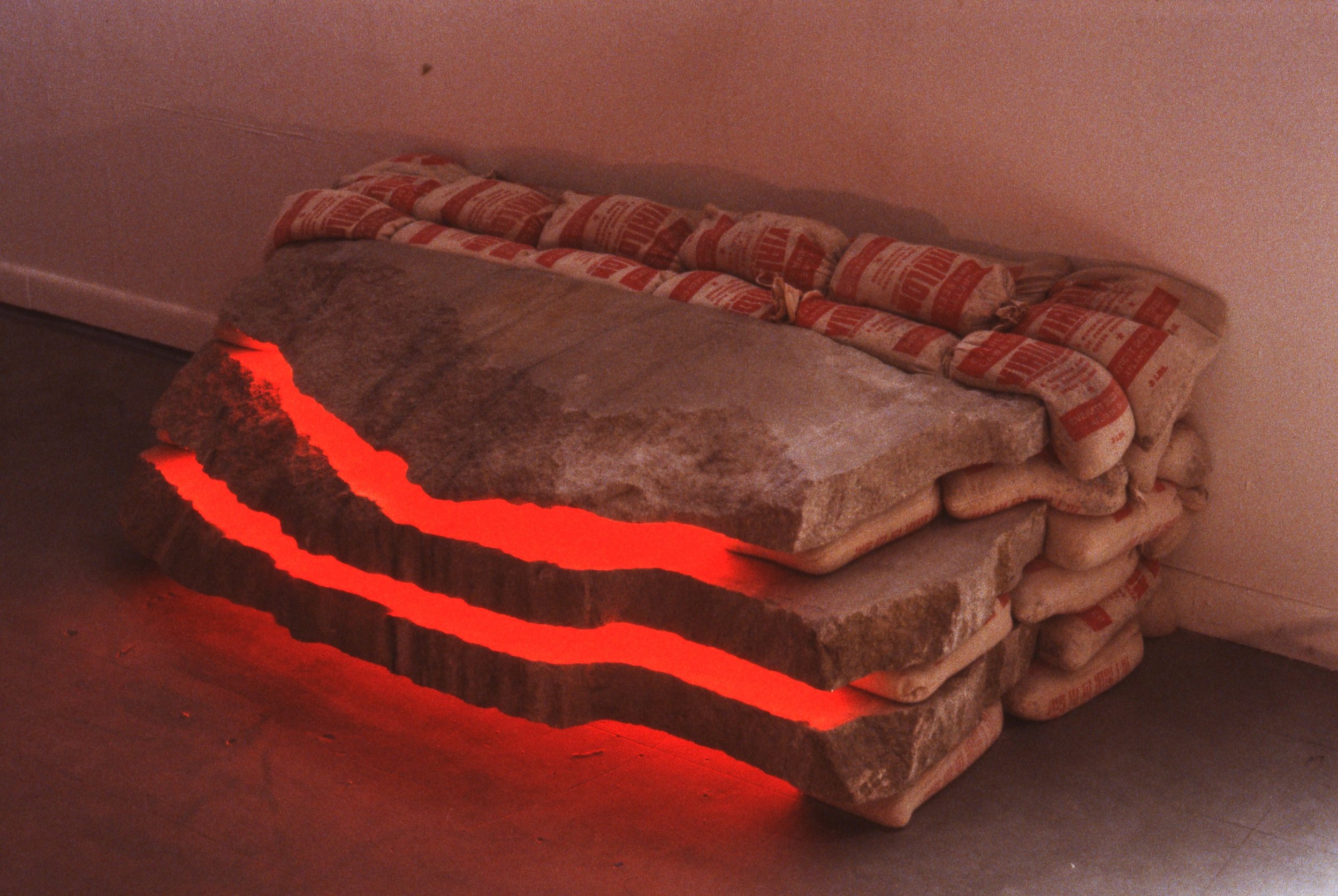 A sculptural piece made of stacked insulation foam sheets with red glowing cracks, resembling a stylized fire or lava, placed on the floor indoors.