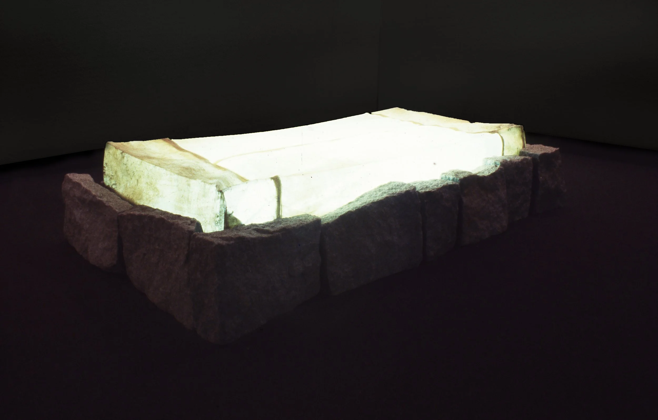 A rectangular stone or marble basin illuminated against a dark background, surrounded by rough stone blocks.