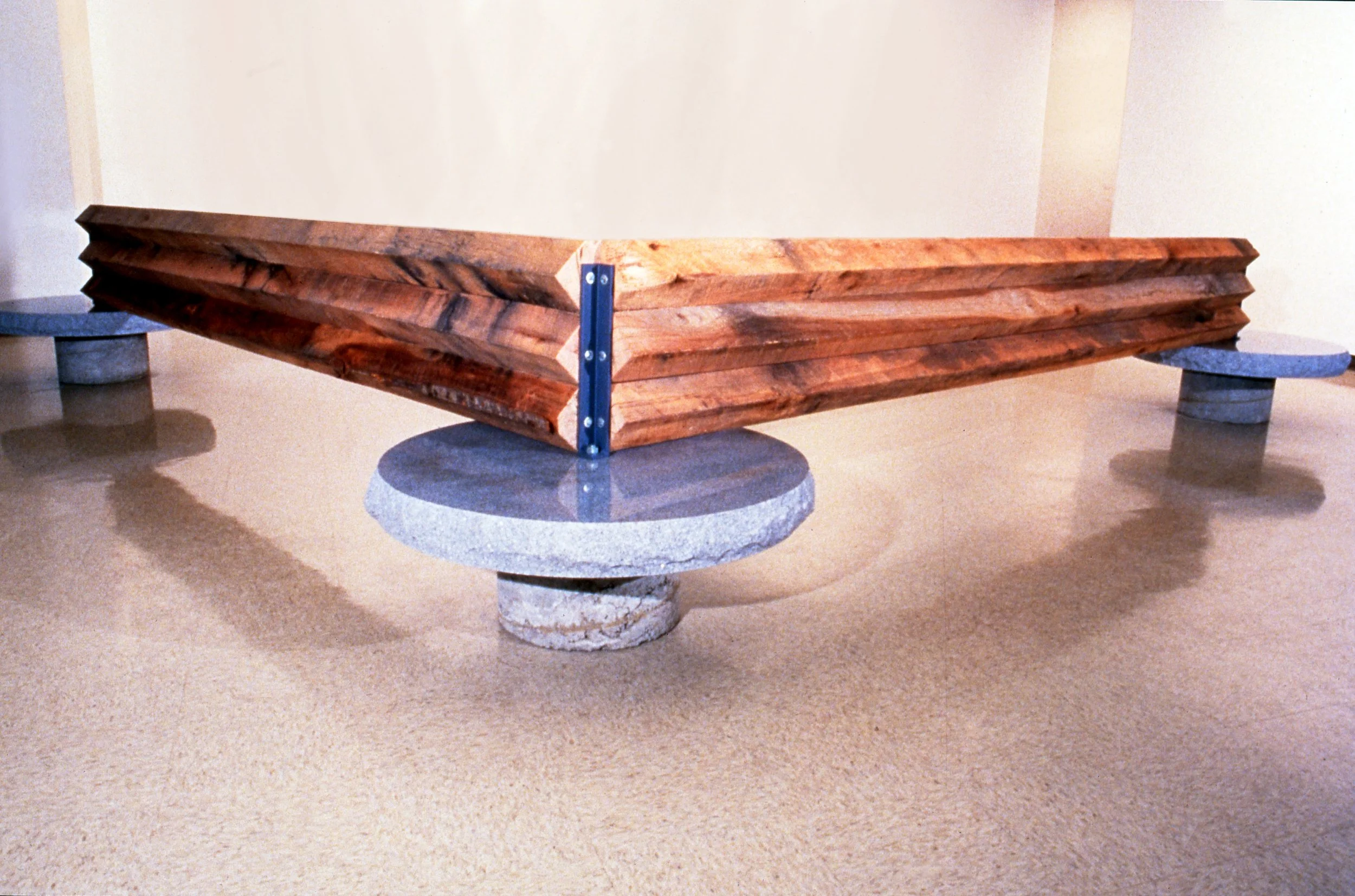A sculpture resembling a wooden boat supported by three stone pedestals.