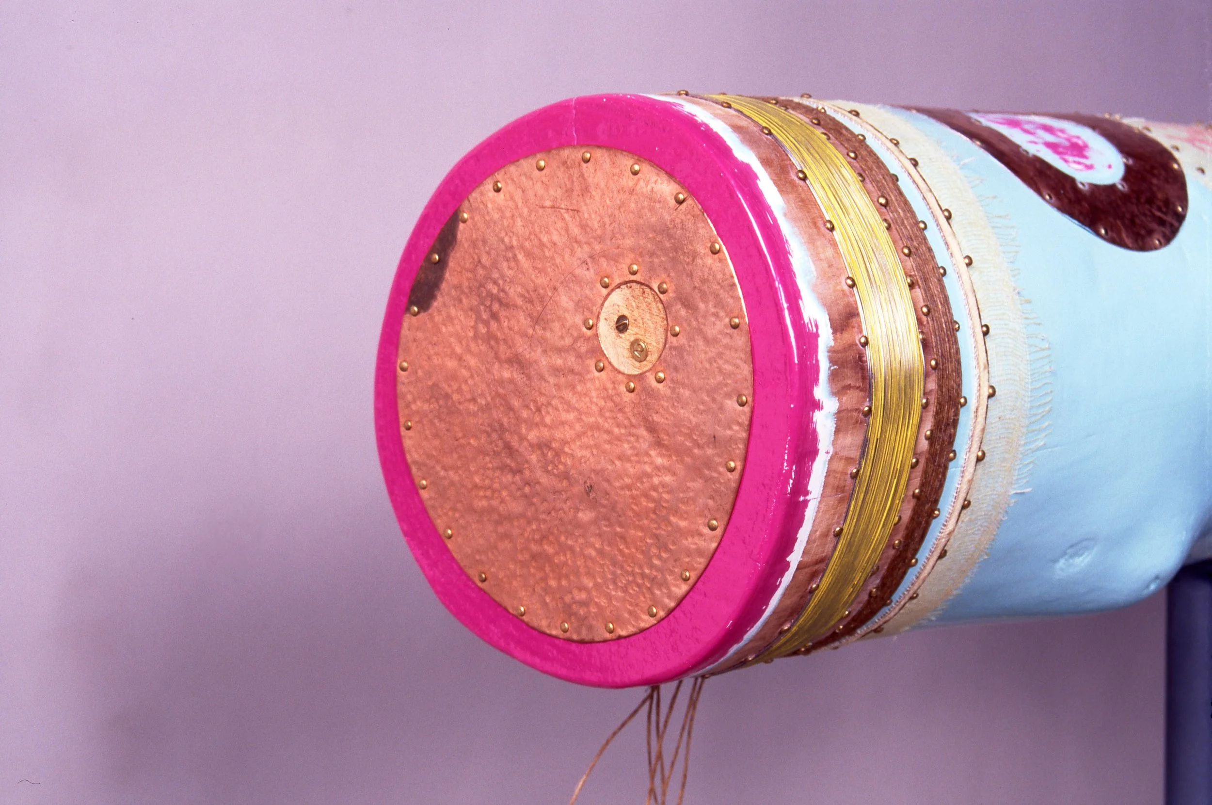 Base of a drum with pink rim, gold and copper accents, and a mixed light blue and beige body, viewed from the bottom.