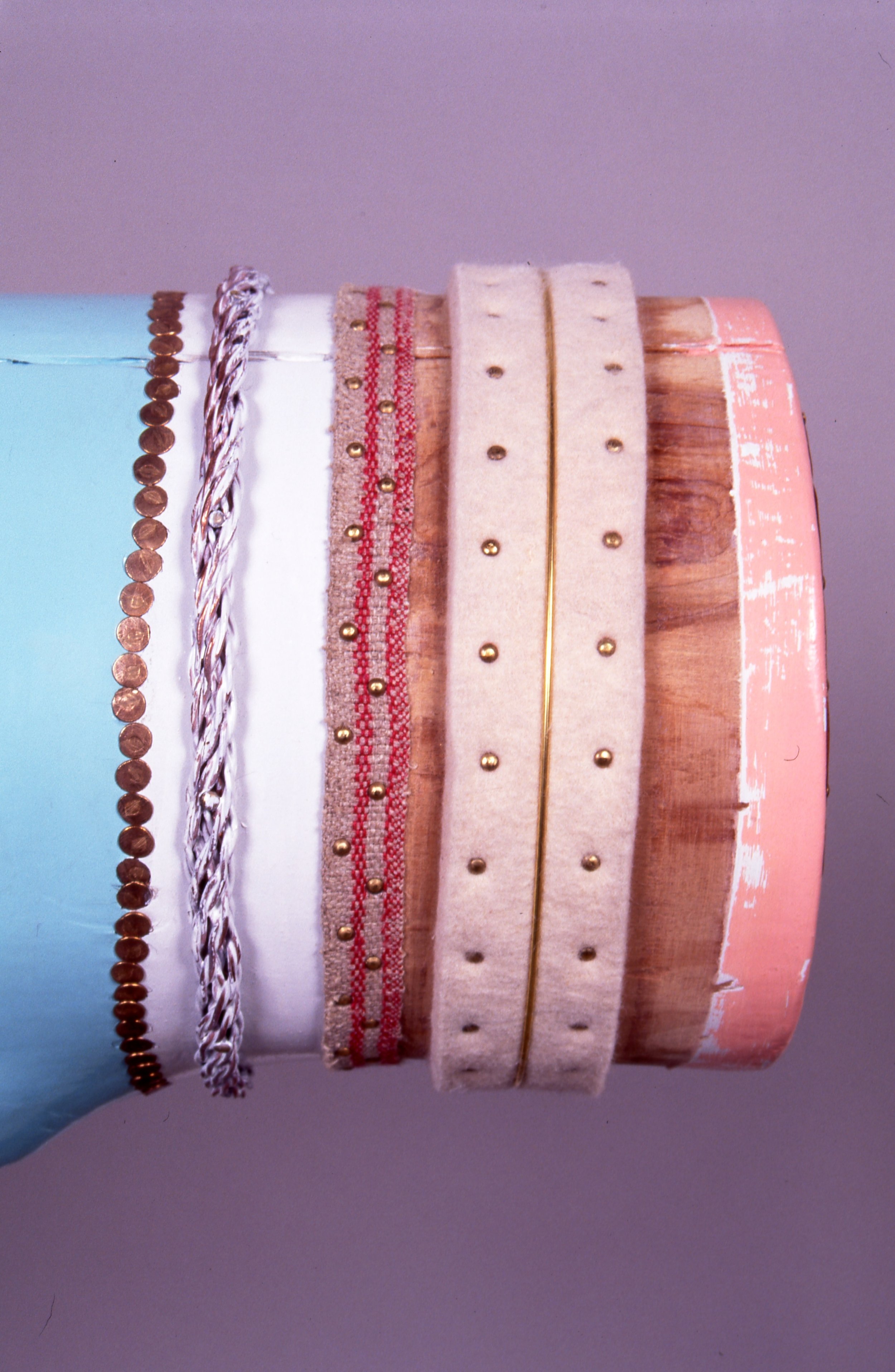 Close-up of a decorated, multi-layered cake with pastel-colored fondant, gold beads, striped ribbon, and an unpainted copper-colored layer.