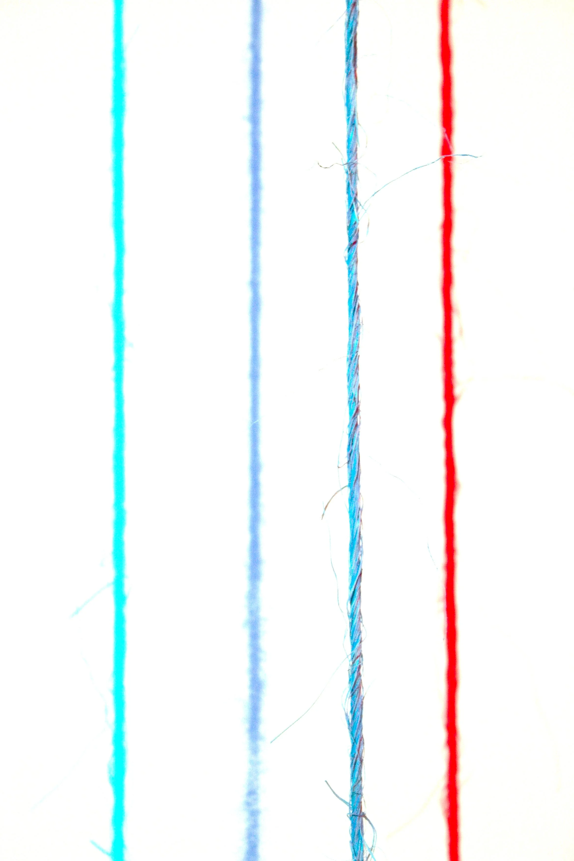 Close-up of four strands of thread in blue, light blue, teal, and red on a white background.