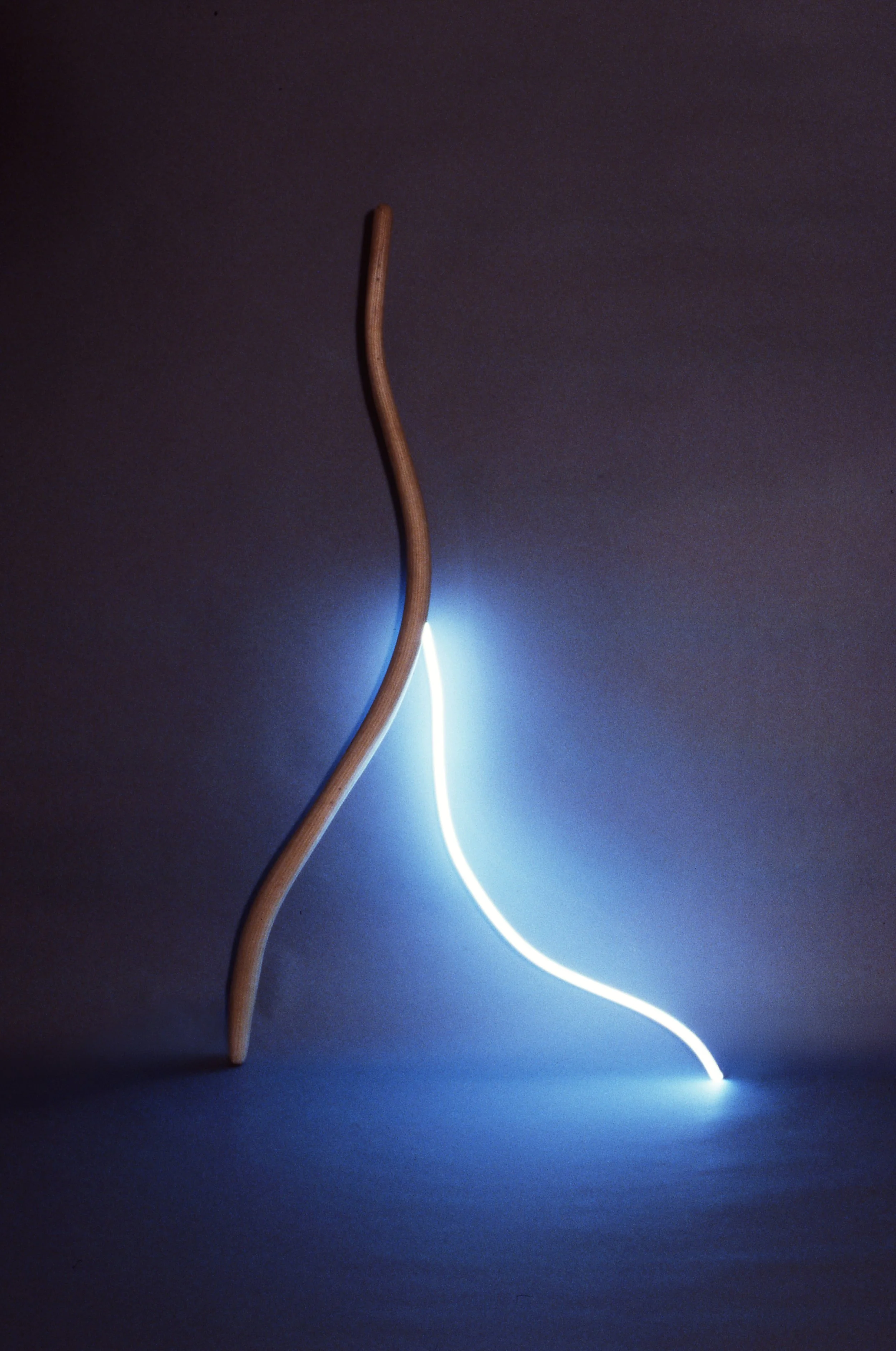 A wooden stick with a curved shape and a glowing white and blue light line on a dark background.