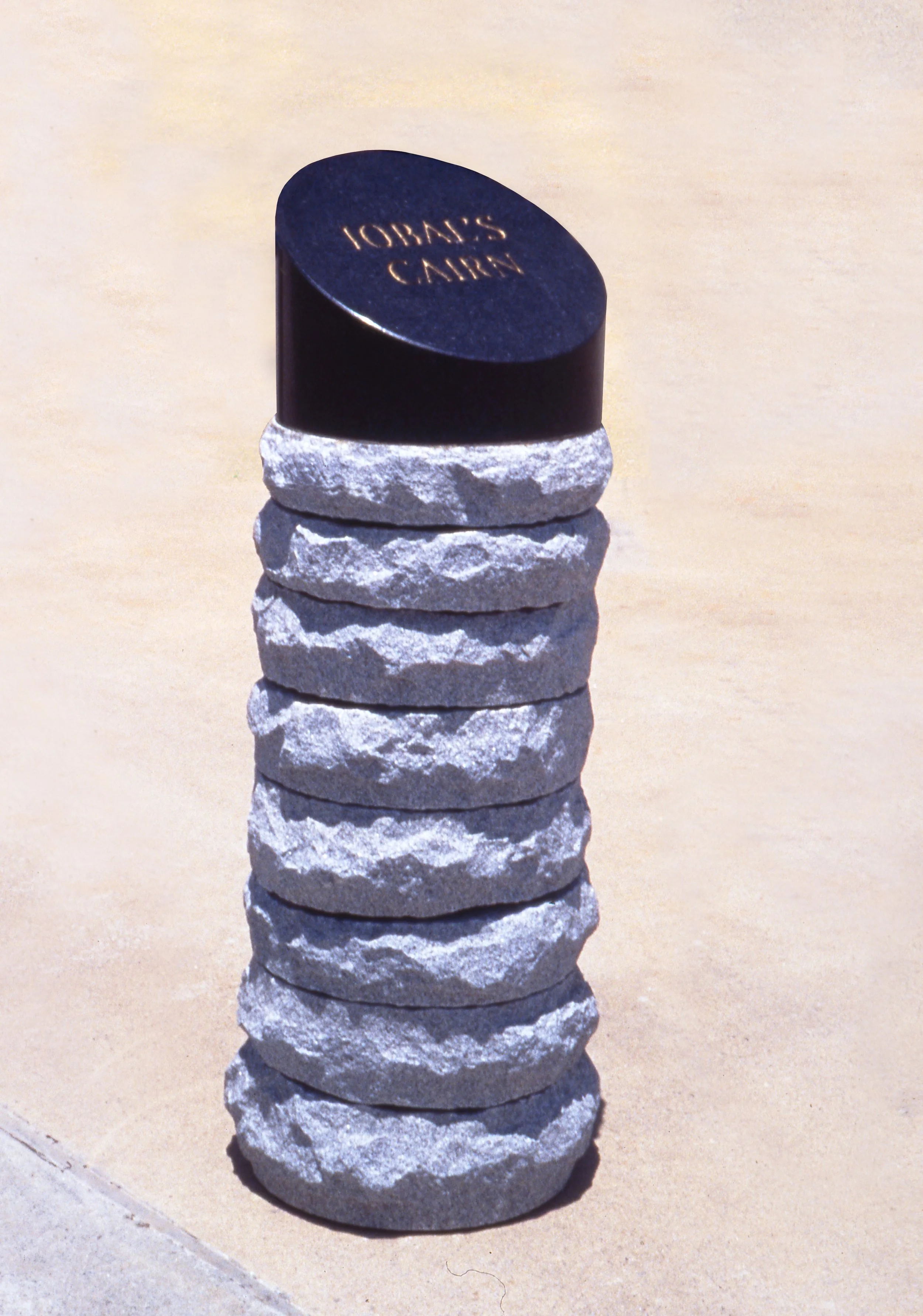 A stack of carved stones with a dark, polished stone on top, engraved with the text 'JOHLAS CAIRN'.
