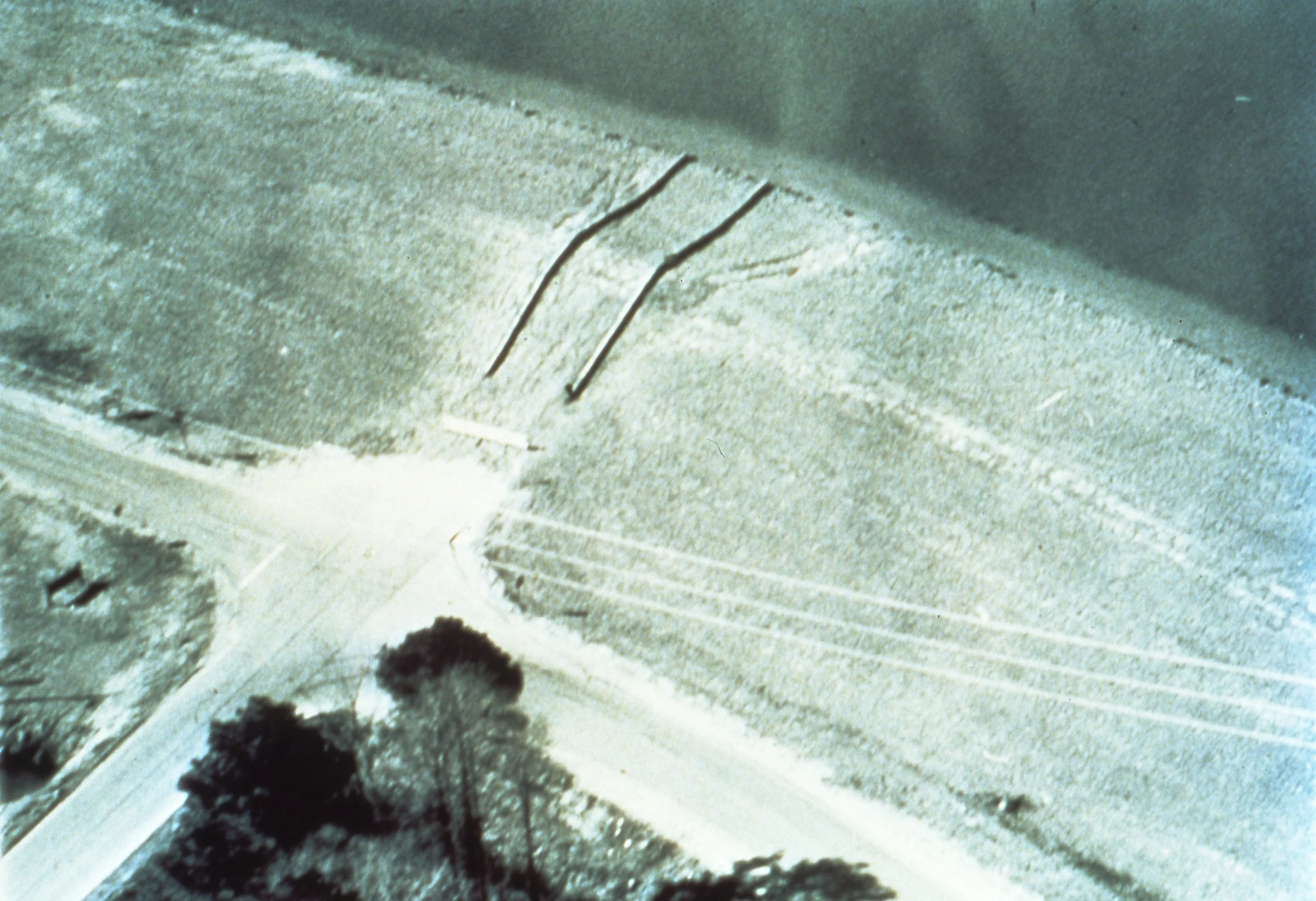 An aerial view of a field intersected by roads, with some trees and utility poles visible along the roads.