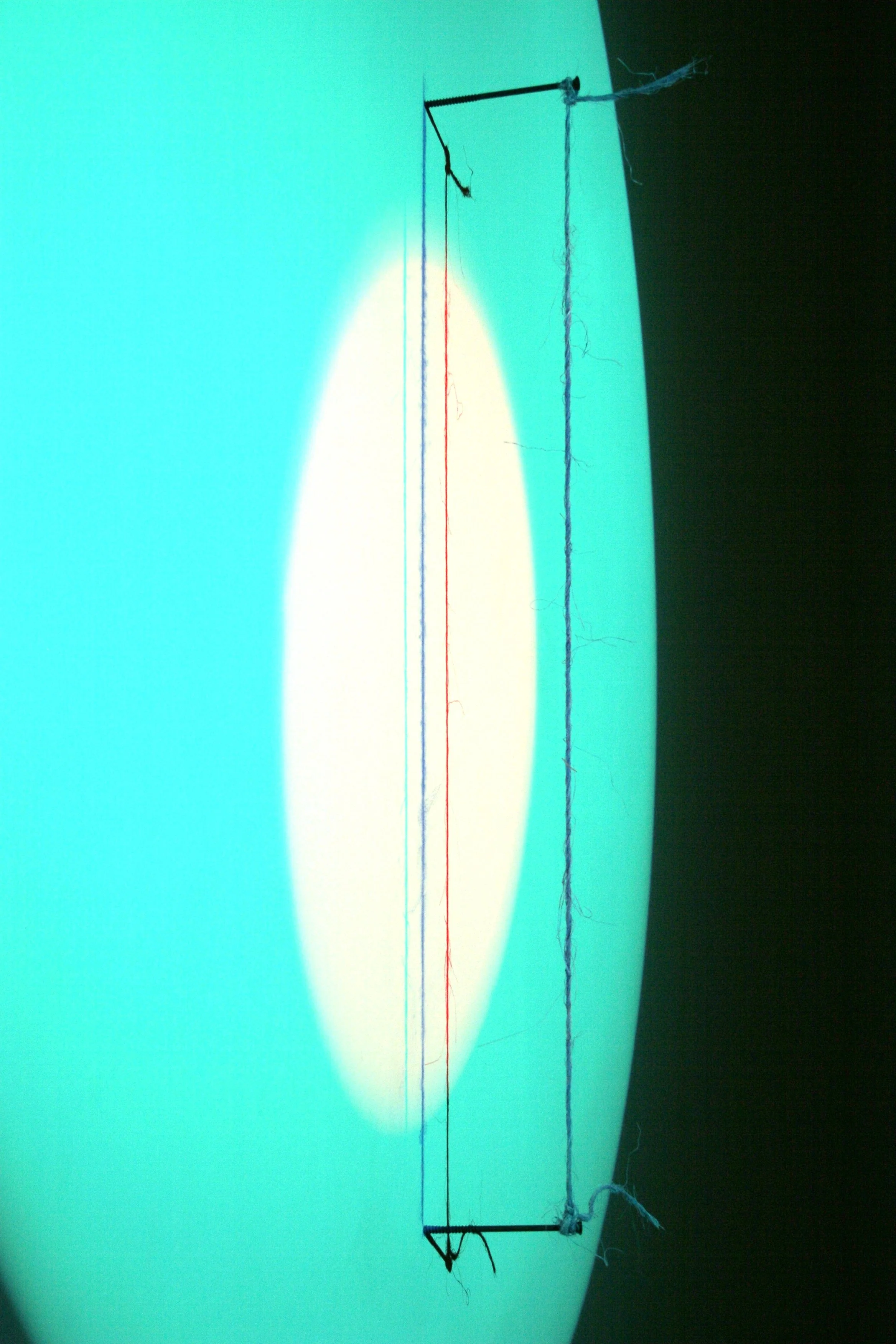 Close-up of a smartphone screen displaying a testing pattern with red, blue, and white colors, and a piece of string attached to a small black frame with a black triangle at one end, against a contrasting teal and black background.