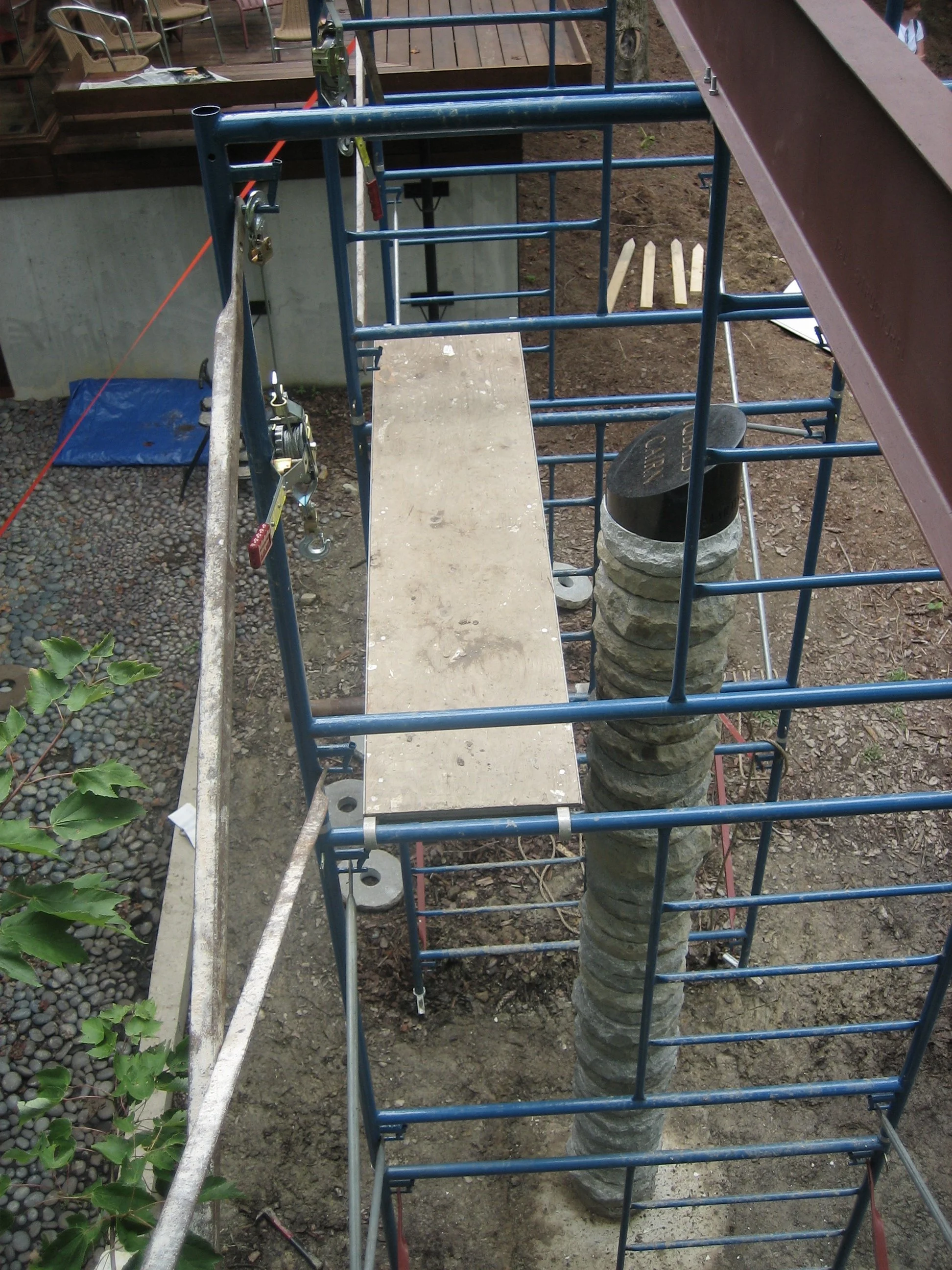 Construction scaffolding surrounding a large tree trunk with layered rings, with a wooden plank on top.